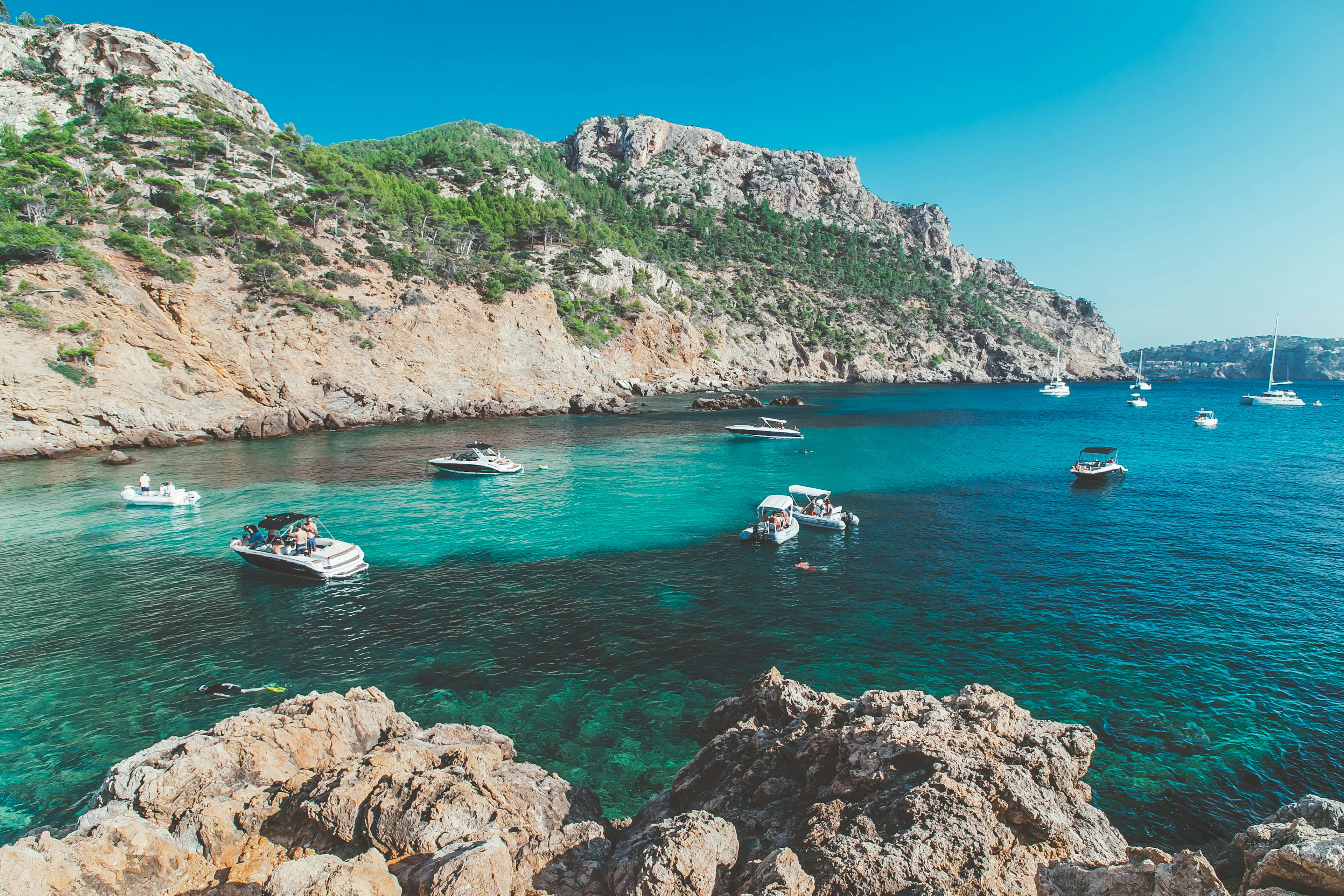 Turquoise waters and rocky cliffs surrounding a secluded coastal cove, with boats anchored along the shoreline.