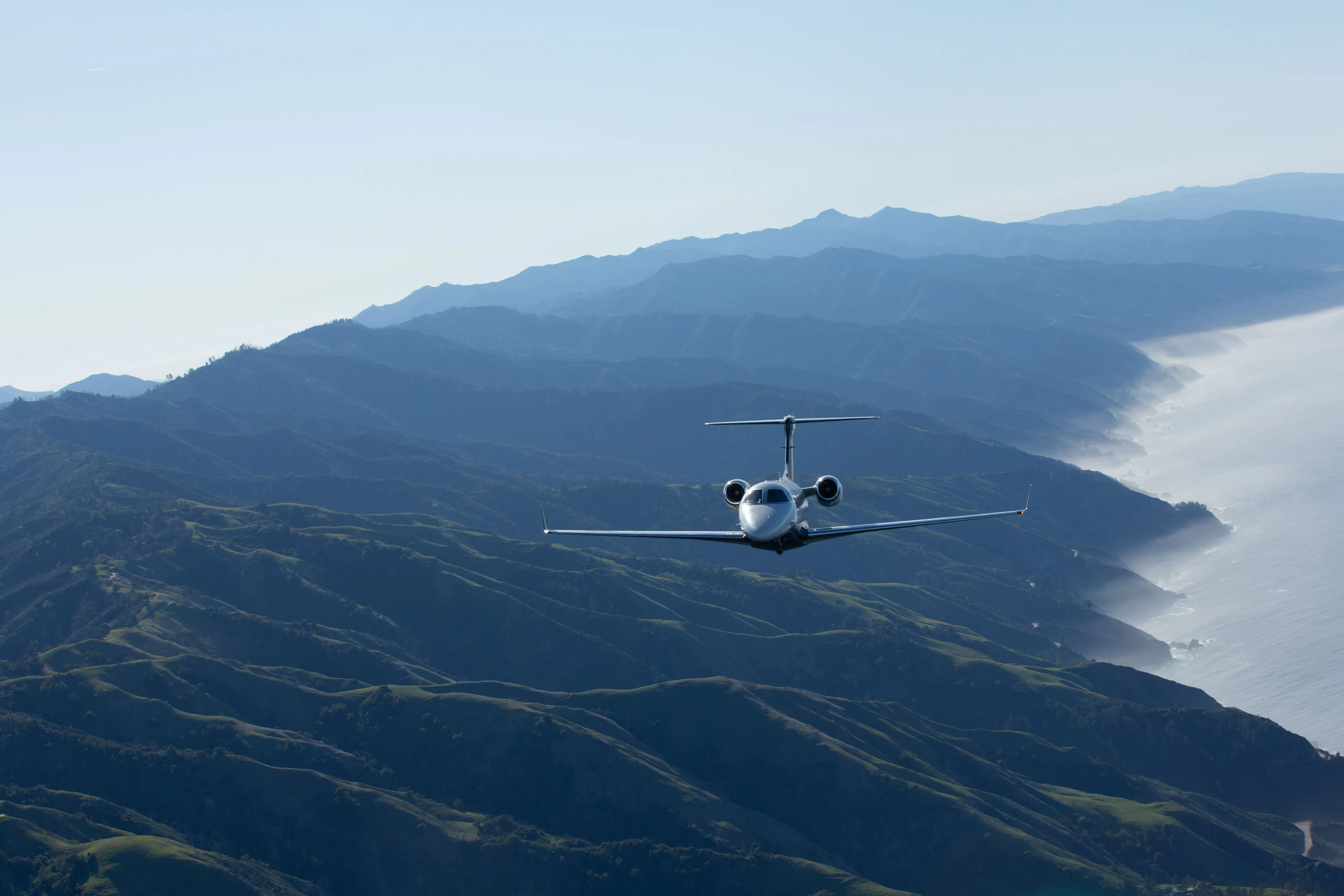 A Phenom 300 flying with mountains and a coastline behind