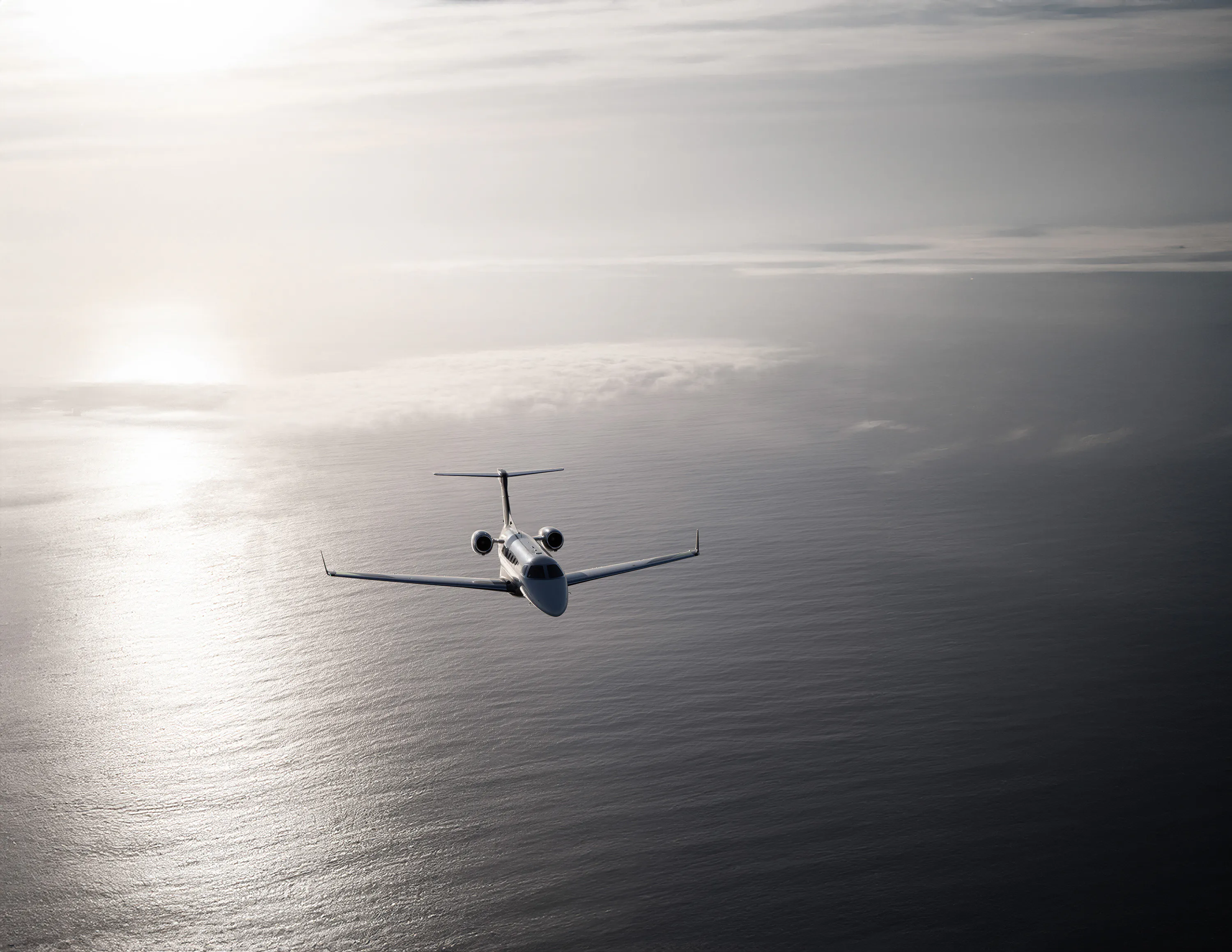 A jet flying forwards over the ocean next to a sunbeam