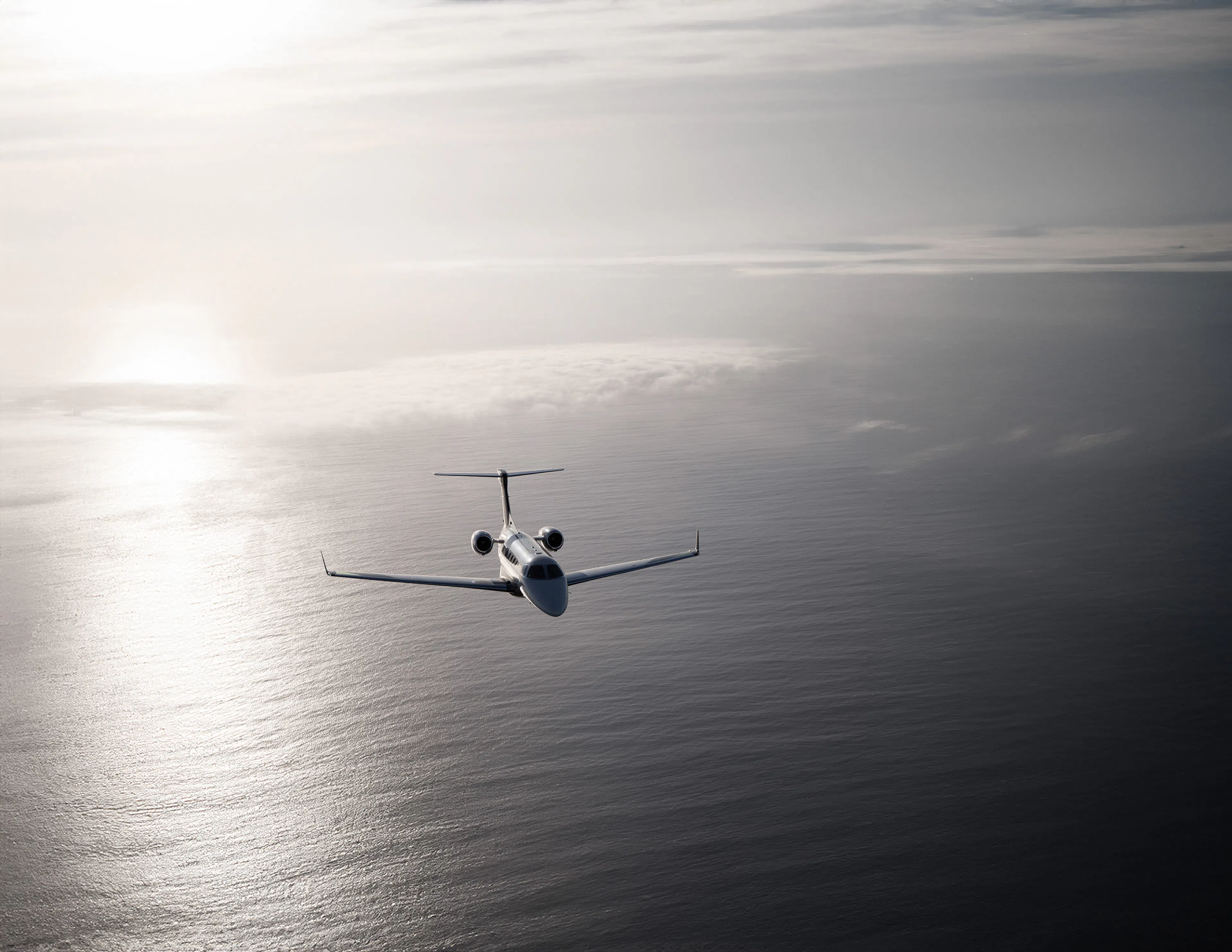 A jet flying forwards over the ocean next to a sunbeam