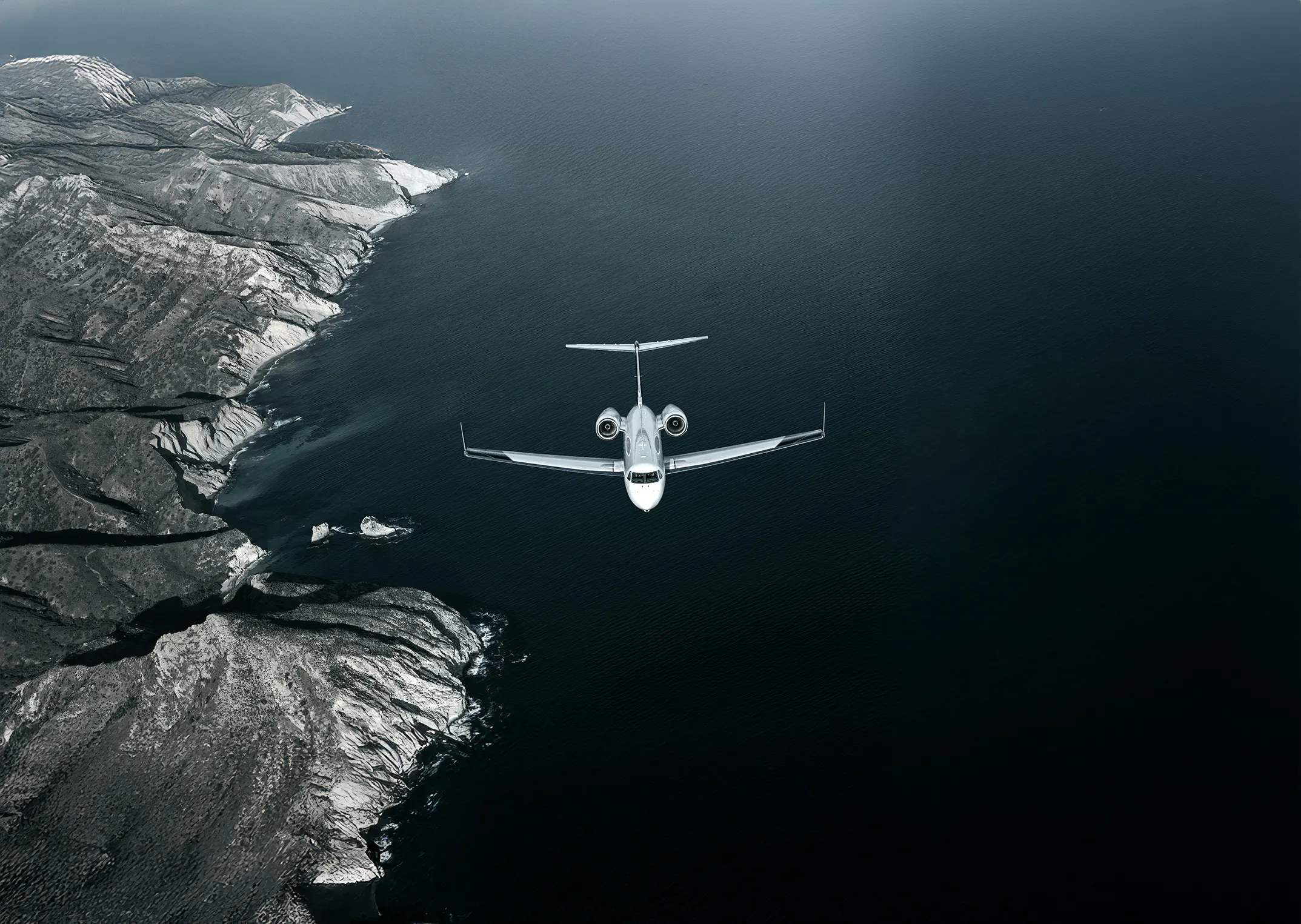 A Gulfstream G450 flying below with the ocean and land below