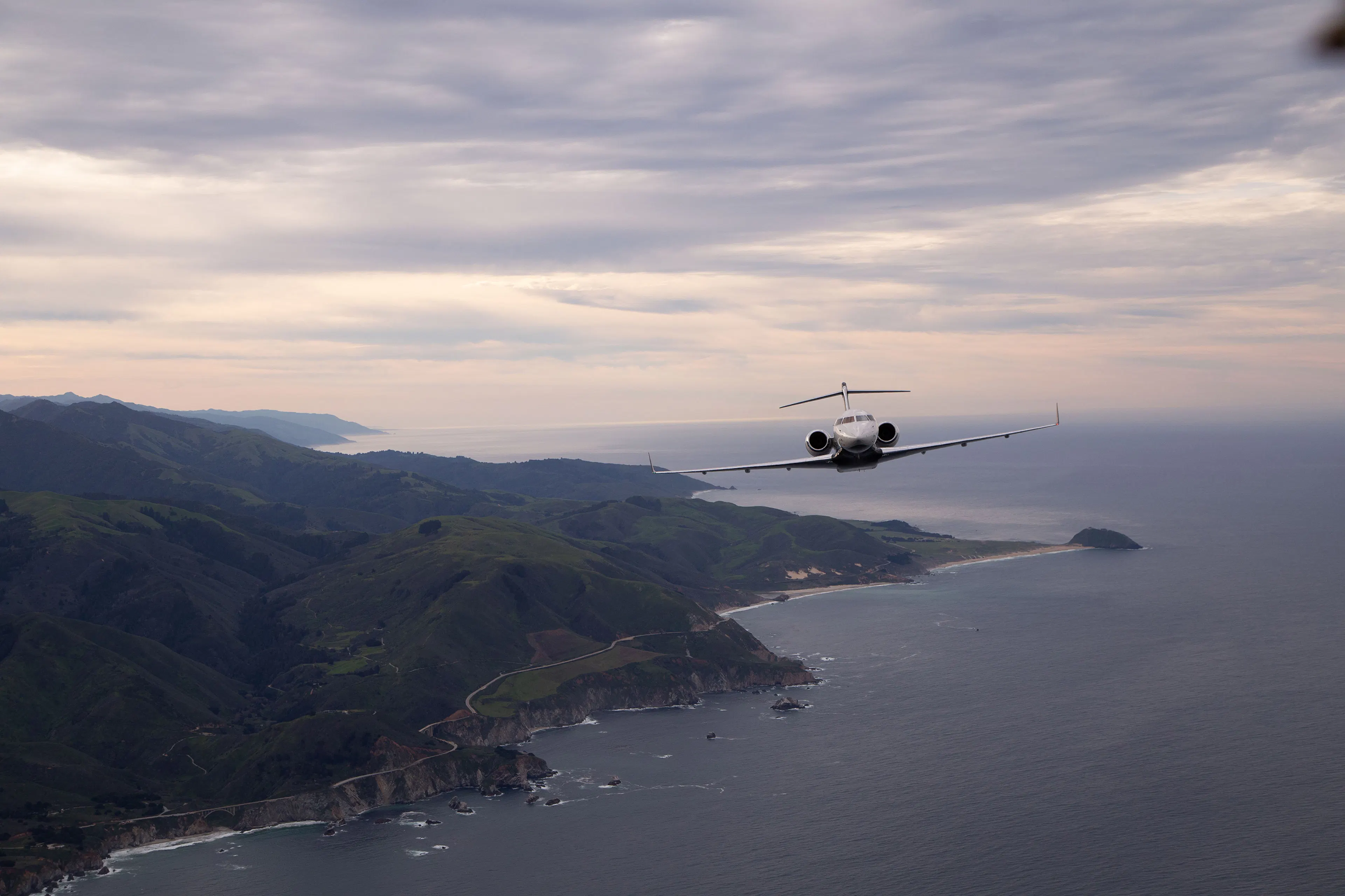 A Global Express Flying over an evening skyline on the ocean with a rugged coastline