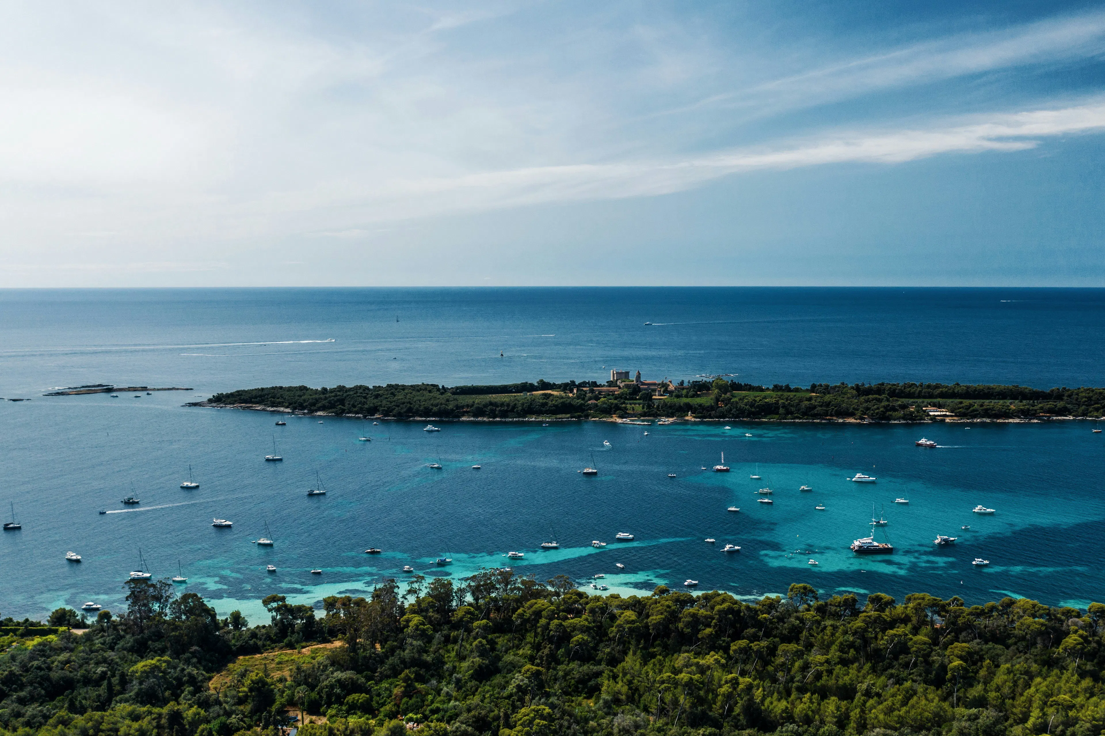 Aerial coastal view near Cannes with turquoise water, boats, a wooded island, and open sea.