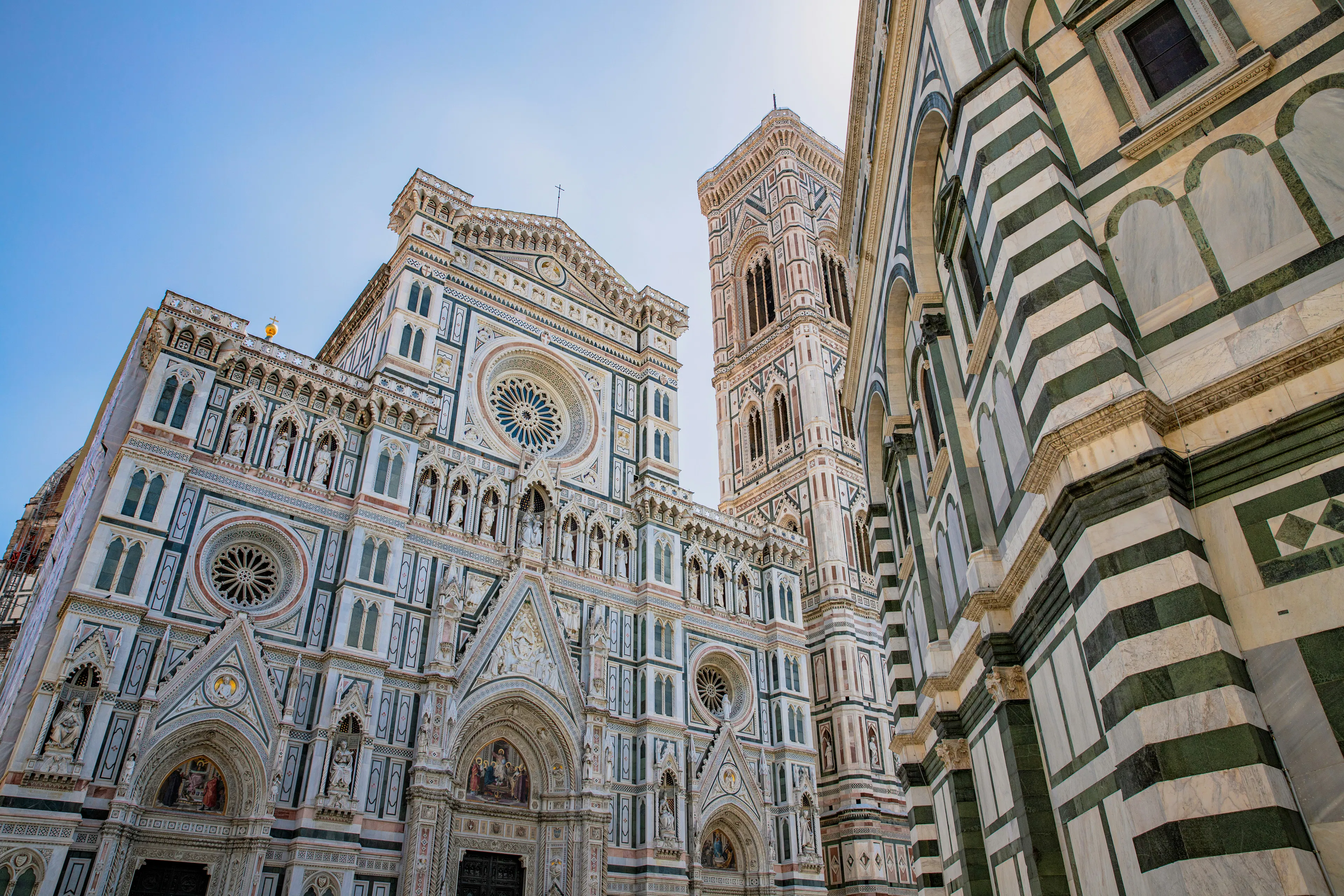 Facade of Florence Cathedral with ornate marble details, arched entrances, and Giotto’s Bell Tower under a clear sky.