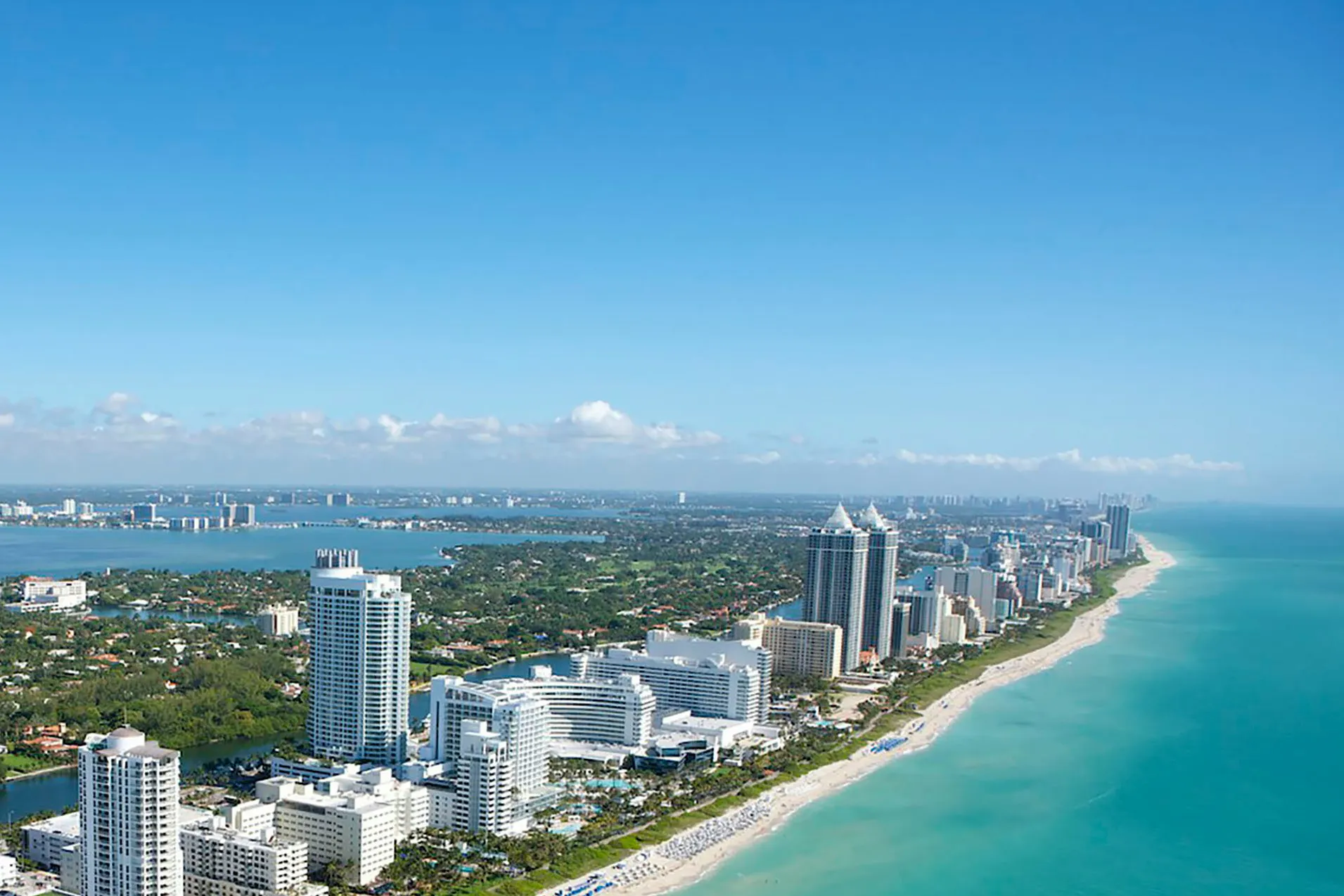 Aerial view of a coastal city with high-rise buildings along a sandy beach and turquoise ocean extending into the distance.