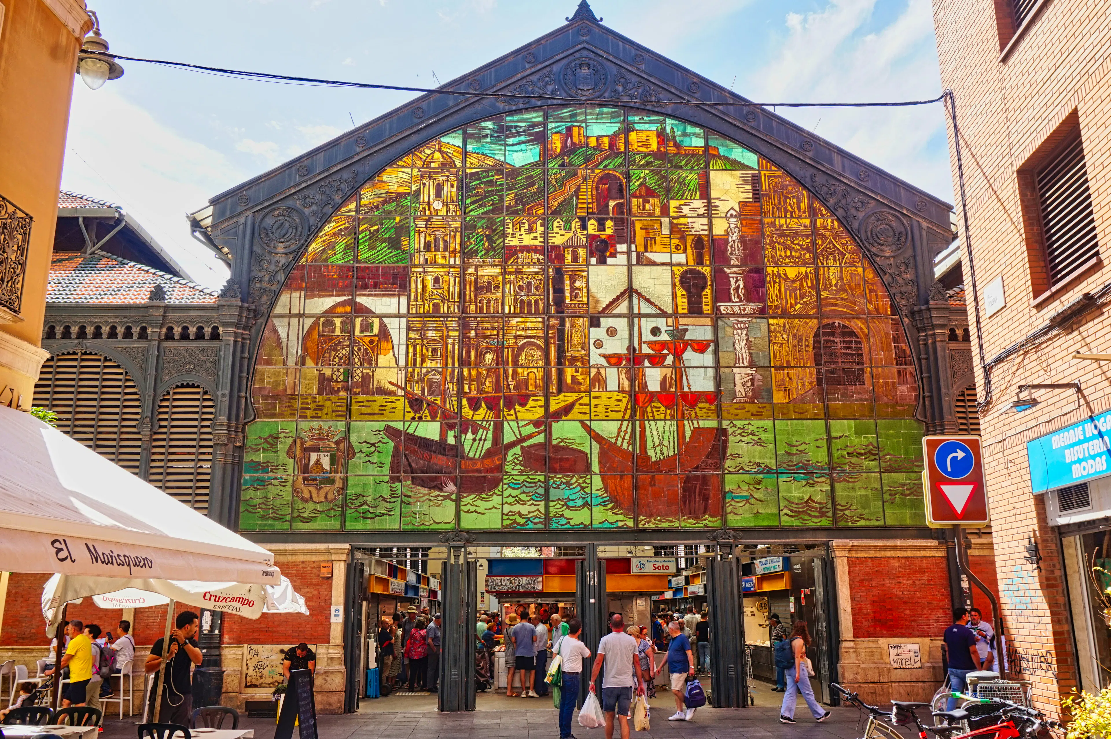 Historic market building featuring a colorful stained-glass façade, surrounded by pedestrians and vibrant city streets.