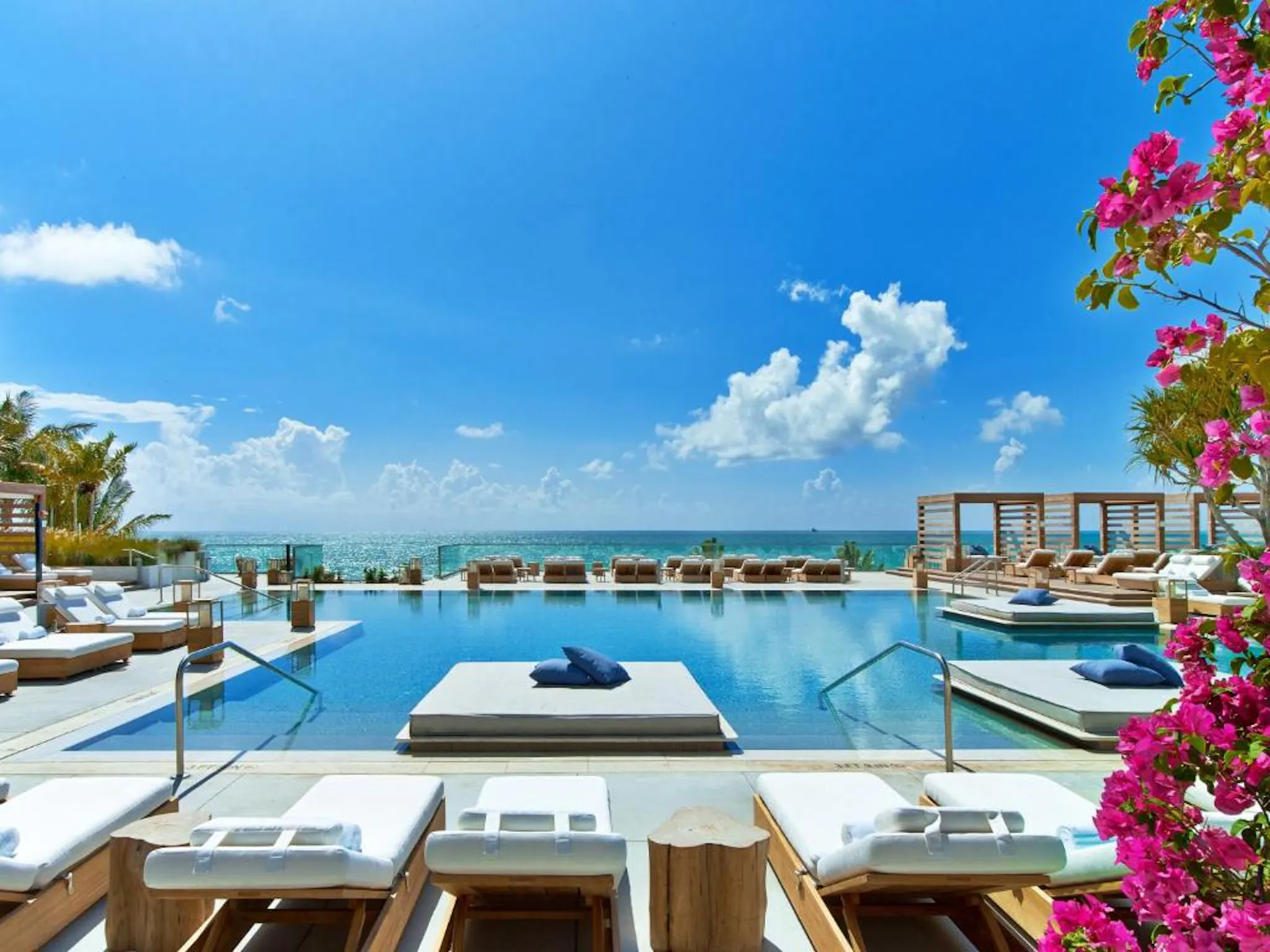 Infinity pool overlooking a calm ocean beneath a bright blue sky.