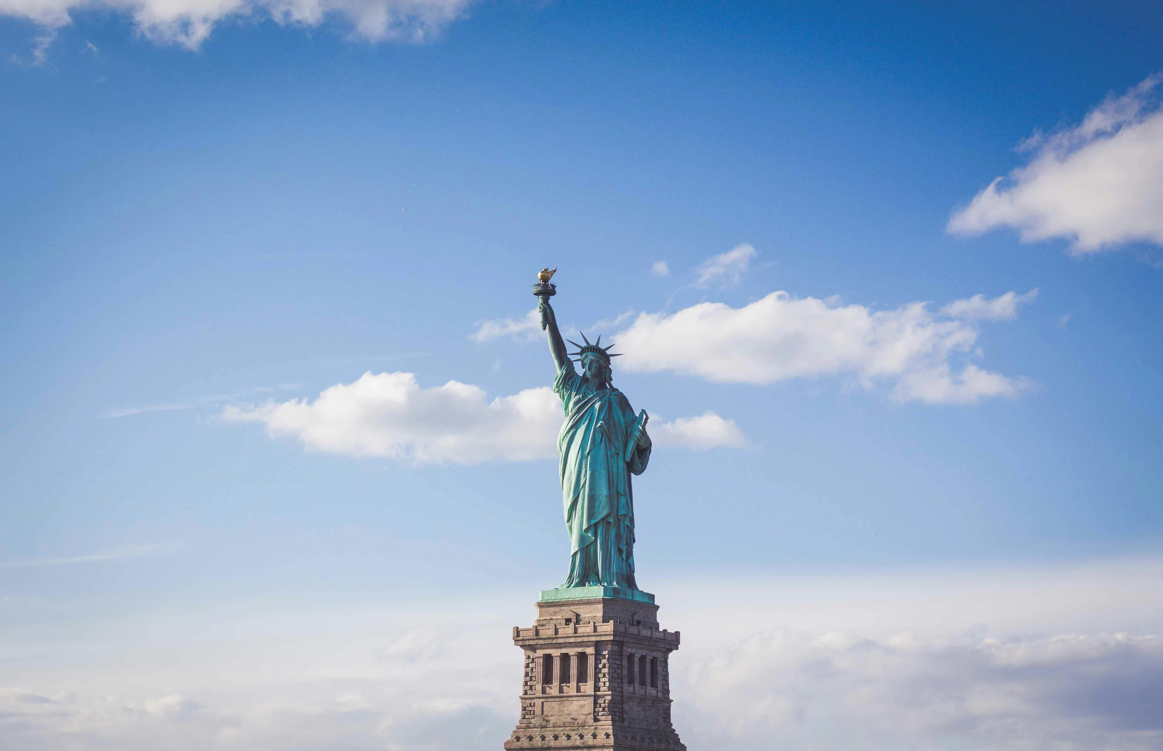 Statue of Liberty in New York Harbor under a blue sky with scattered clouds.