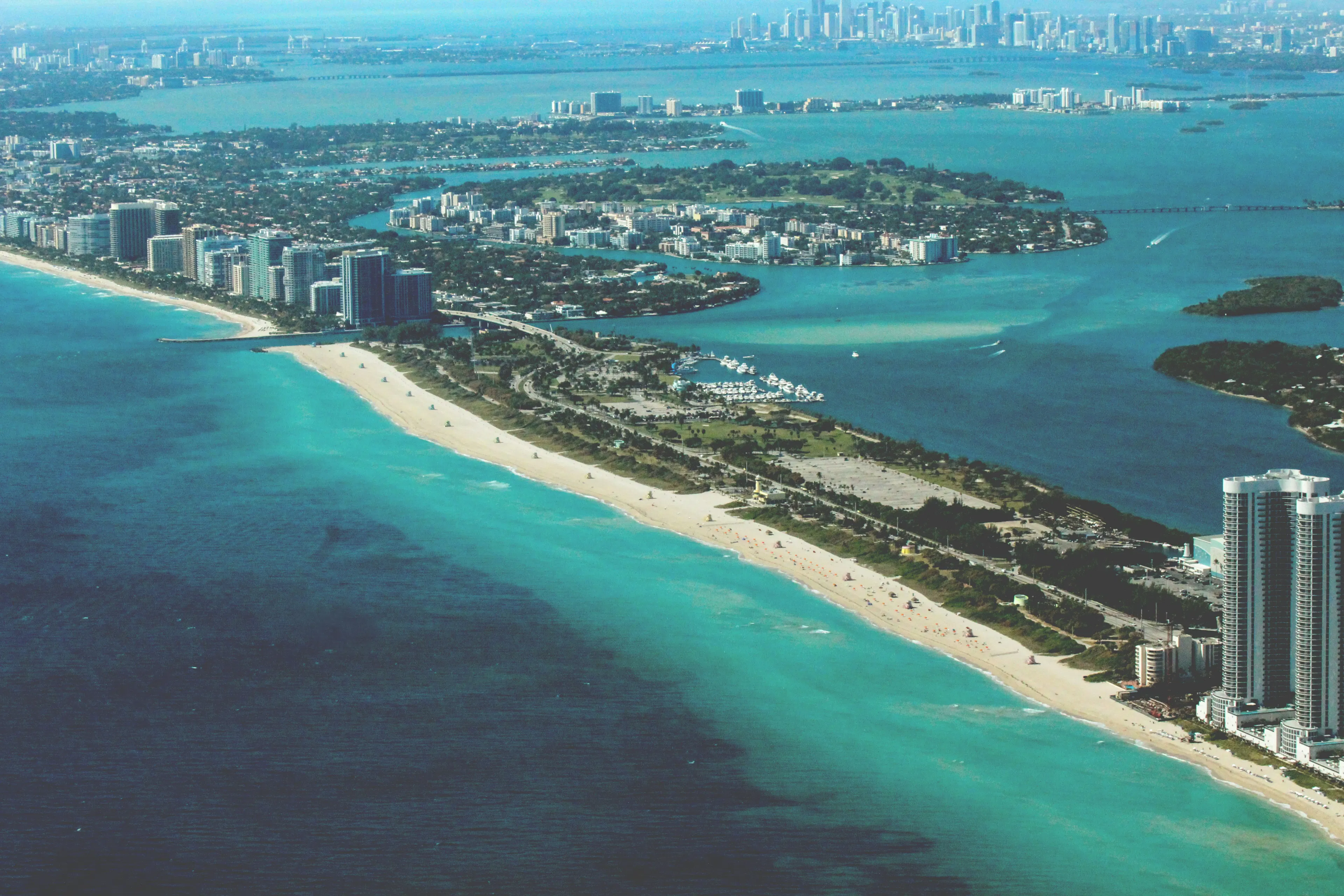 Aerial view of Miami Beach with turquoise water, sandy coastline, islands, and city buildings.