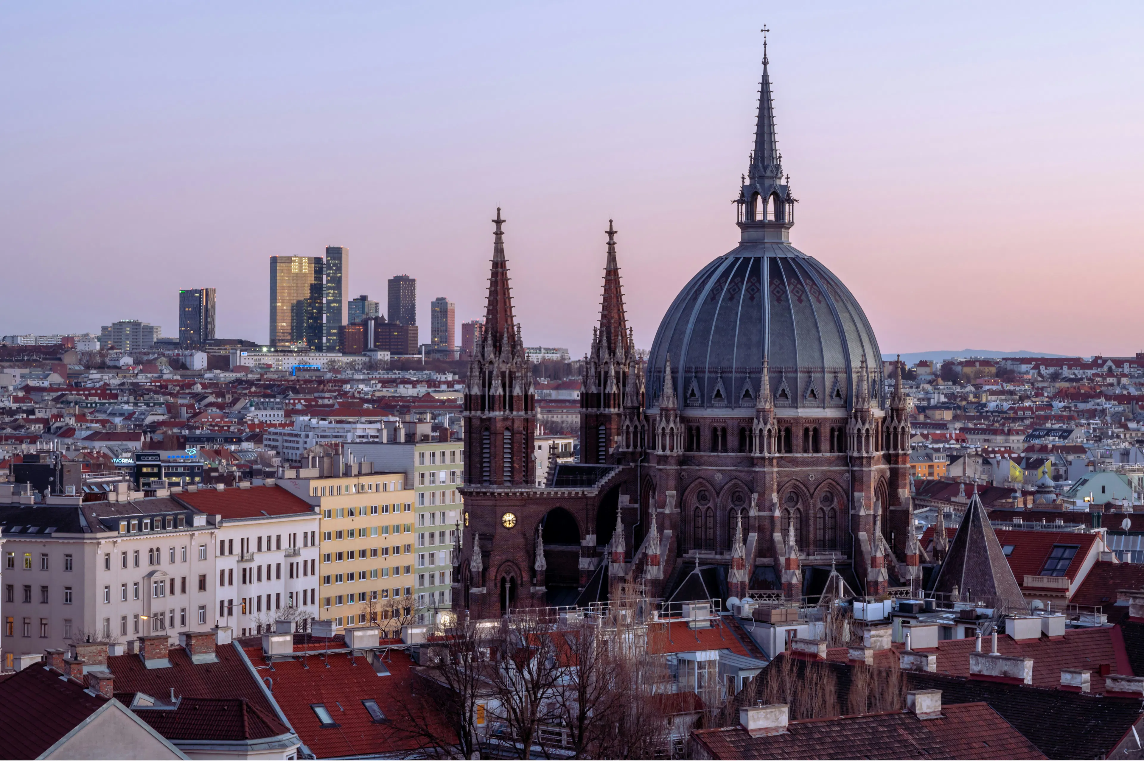Vienna skyline at dusk with a large domed church, red rooftops, and modern buildings in the distance.