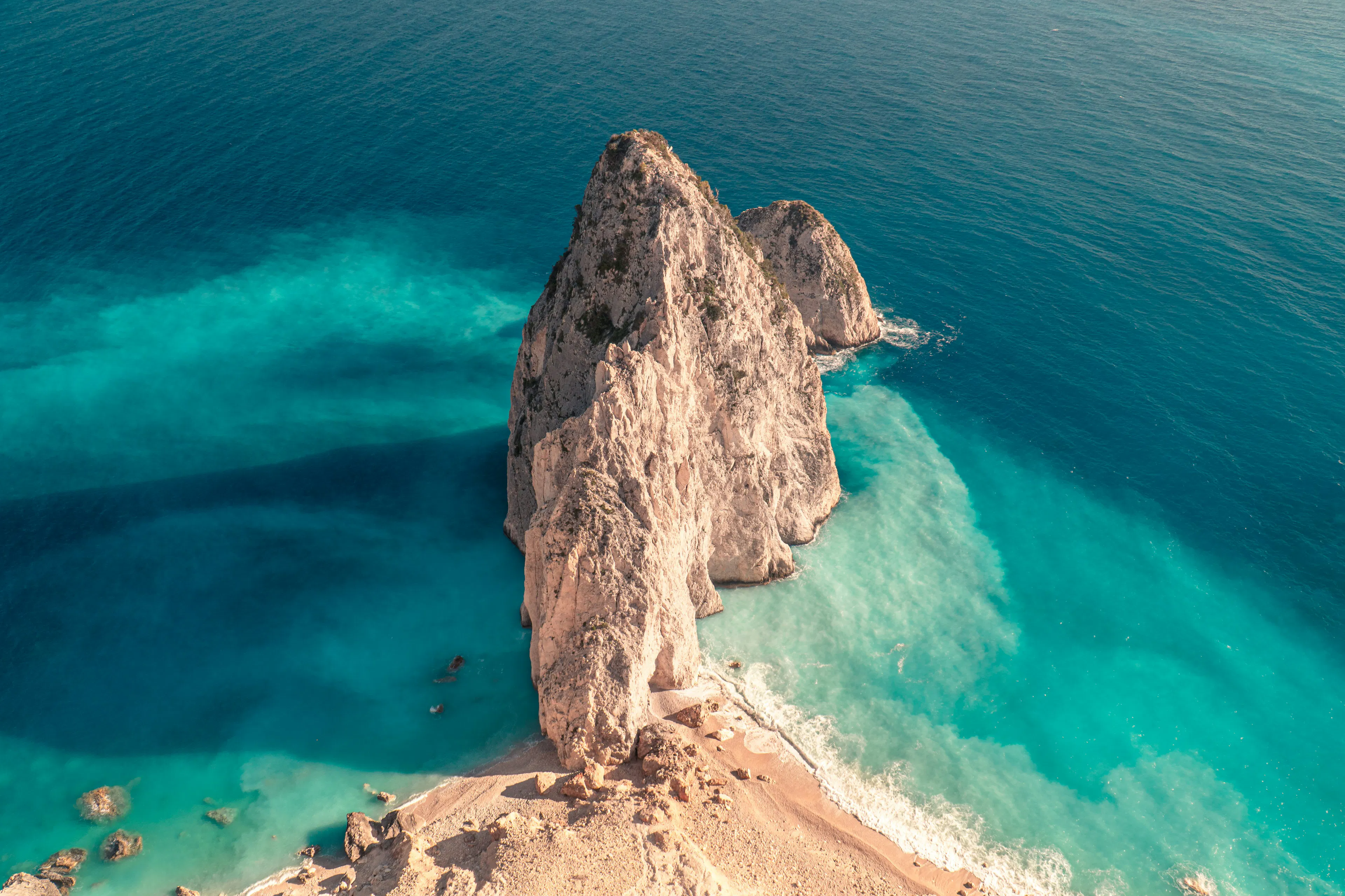 Dramatic coastal rock formation surrounded by crystal-clear turquoise waters along the Aegean shoreline.