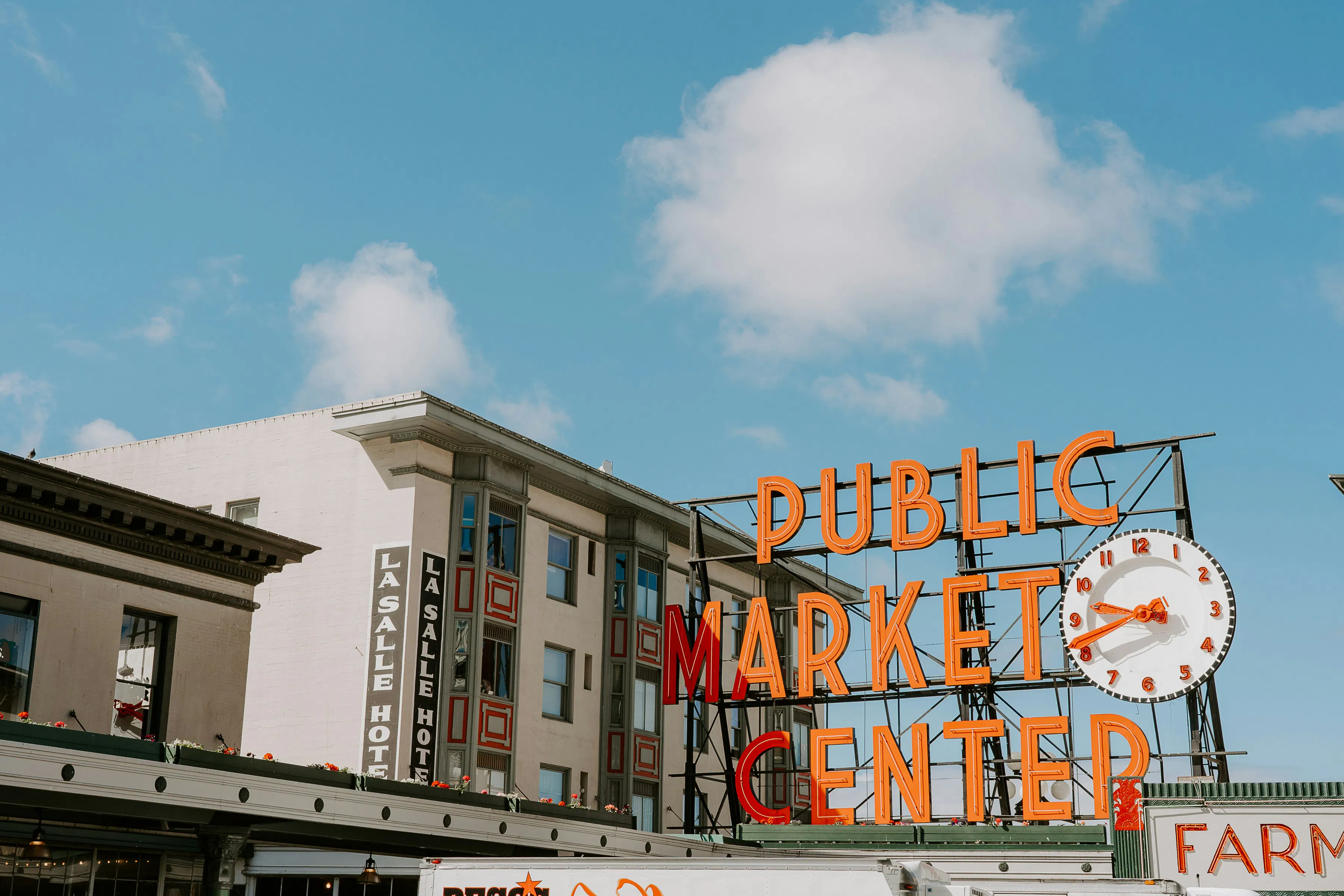 Public Market Center sign and clock above Pike Place Market buildings under a blue sky.