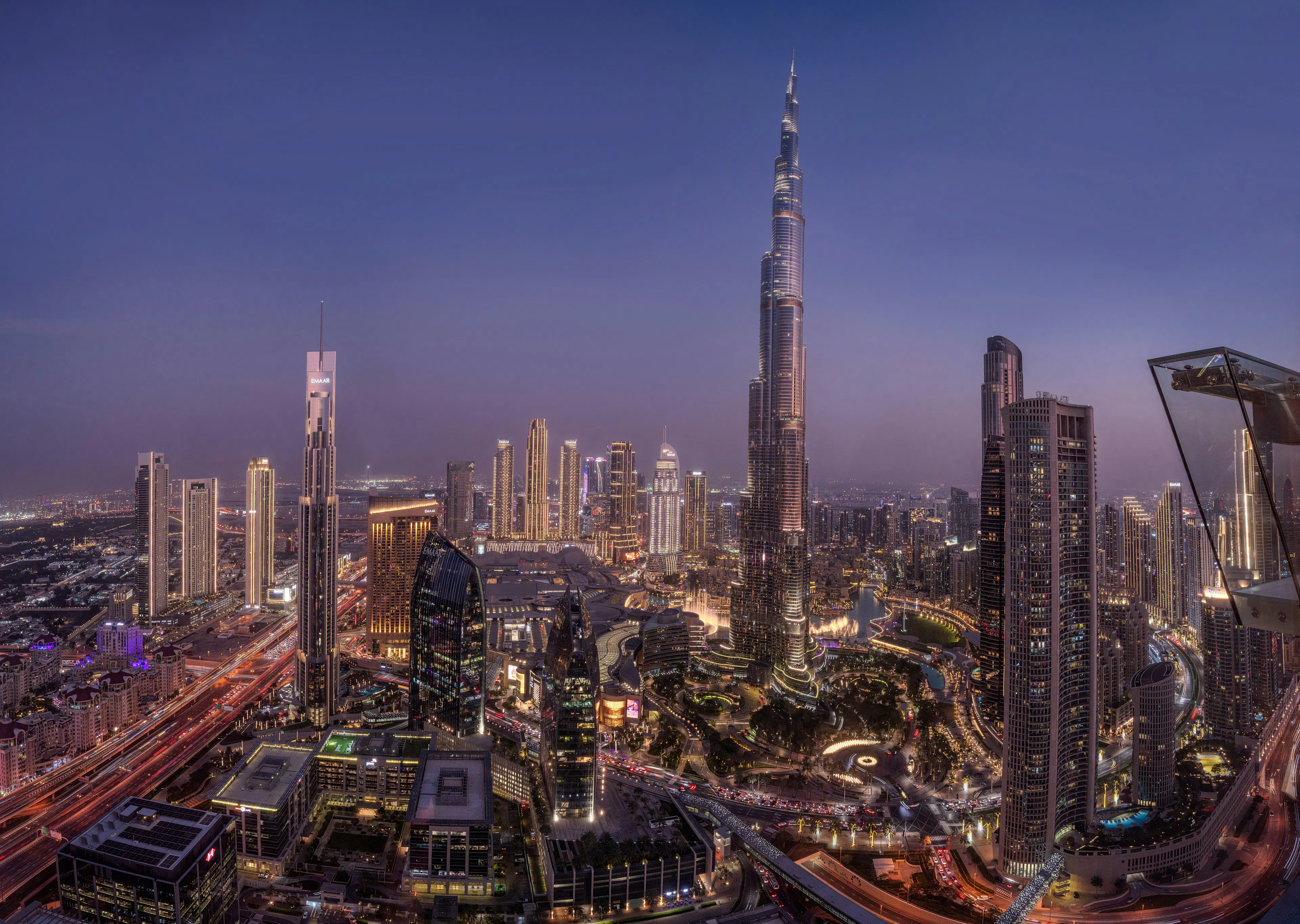 Dubai skyline at night with the Burj Khalifa surrounded by illuminated high-rise buildings and city roads.