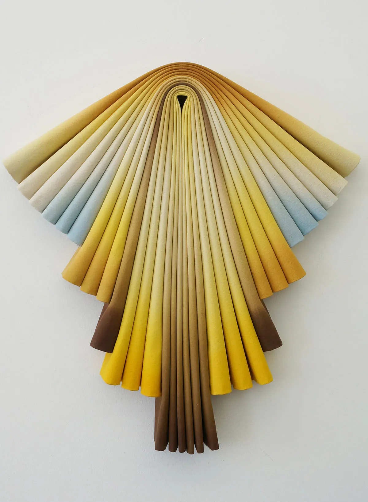 Susan Maddux’s Sol, a pleated acrylic-on-canvas wall relief radiating in golden yellow, ochre, cream and pale sky blue, with a brown tapered base.