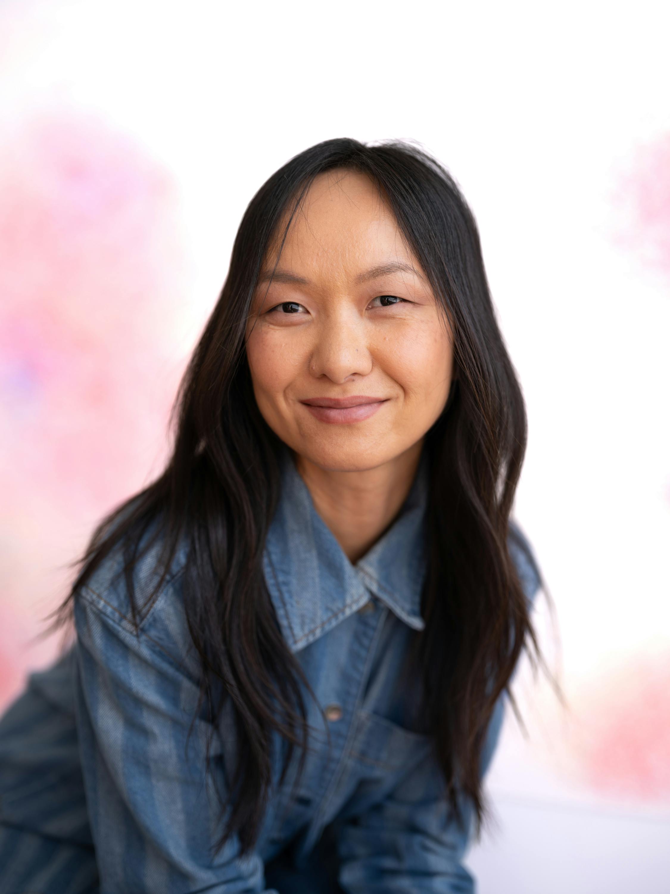 Portrait of artist Sheng Lor standing in front of her abstract drawings, wearing a blue denim outfit.
