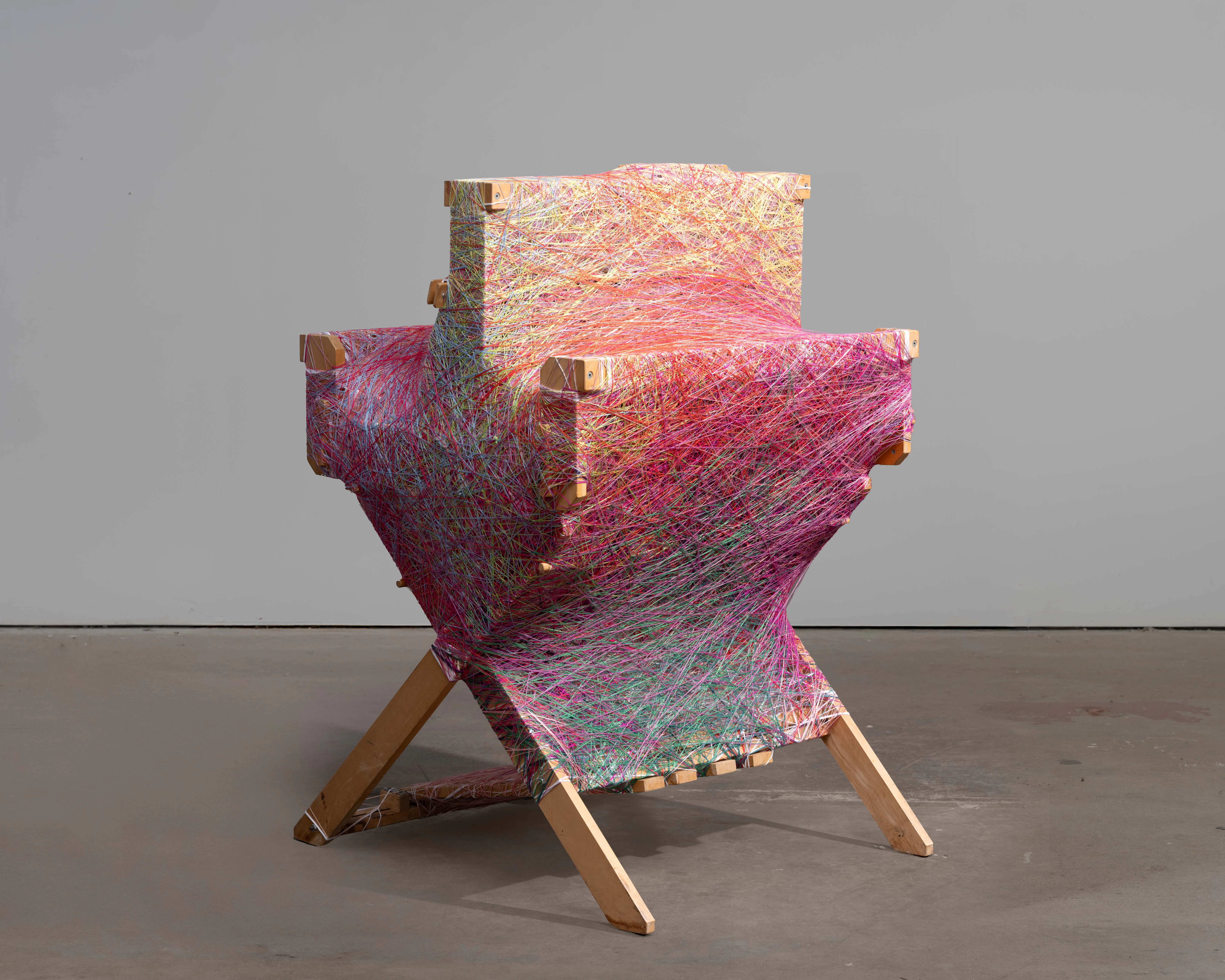 Sheng Lor, Loom 4, 2025 — dressed loom sculpture constructed from a wooden loom wrapped in layered pink, red, green, and yellow yarns, standing on angled wooden legs.