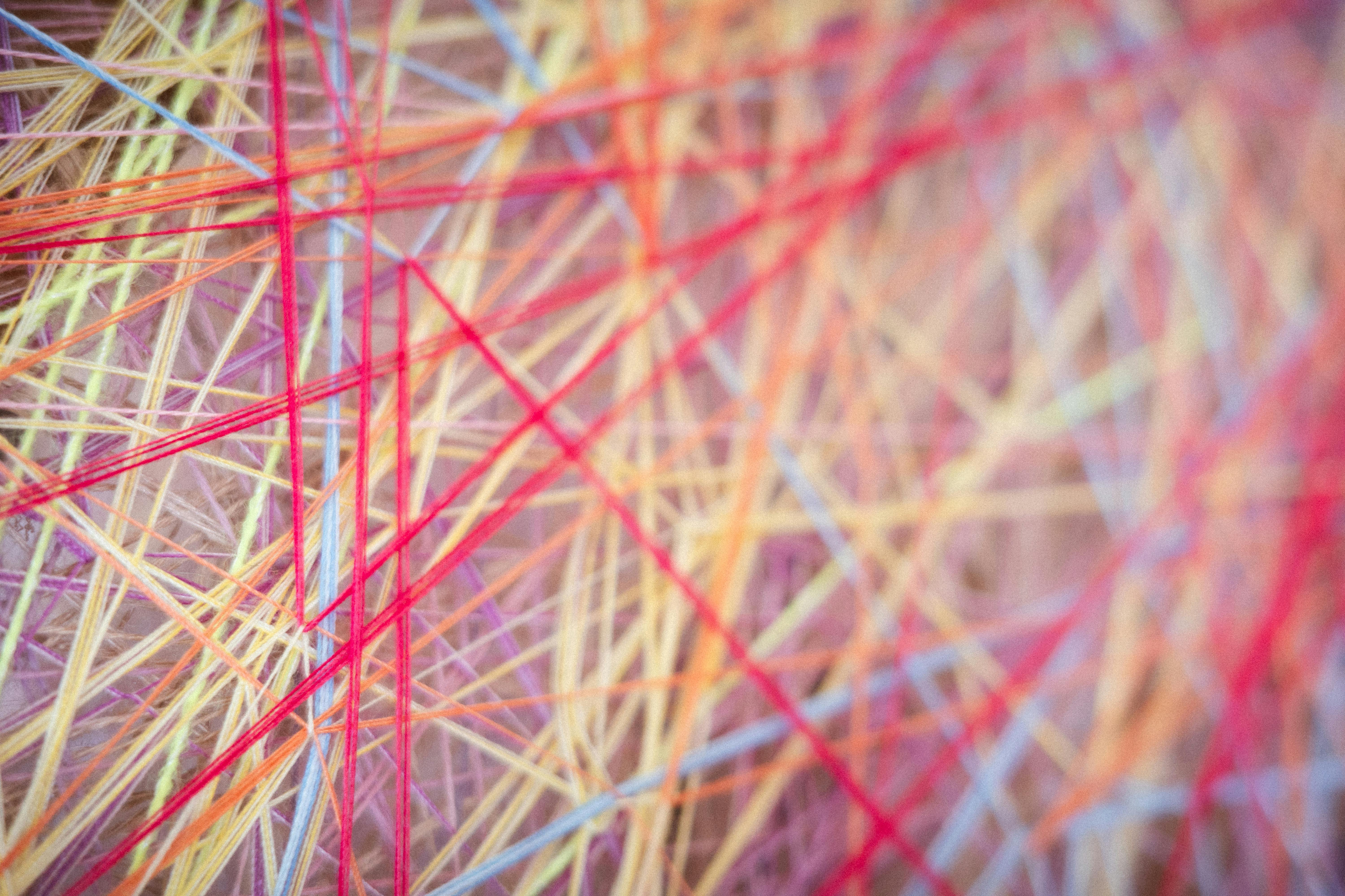 Close-up of intersecting multicolored yarns stretched across Sheng Lor’s Loom 4, showing red threads crossing softer pastel fibers.