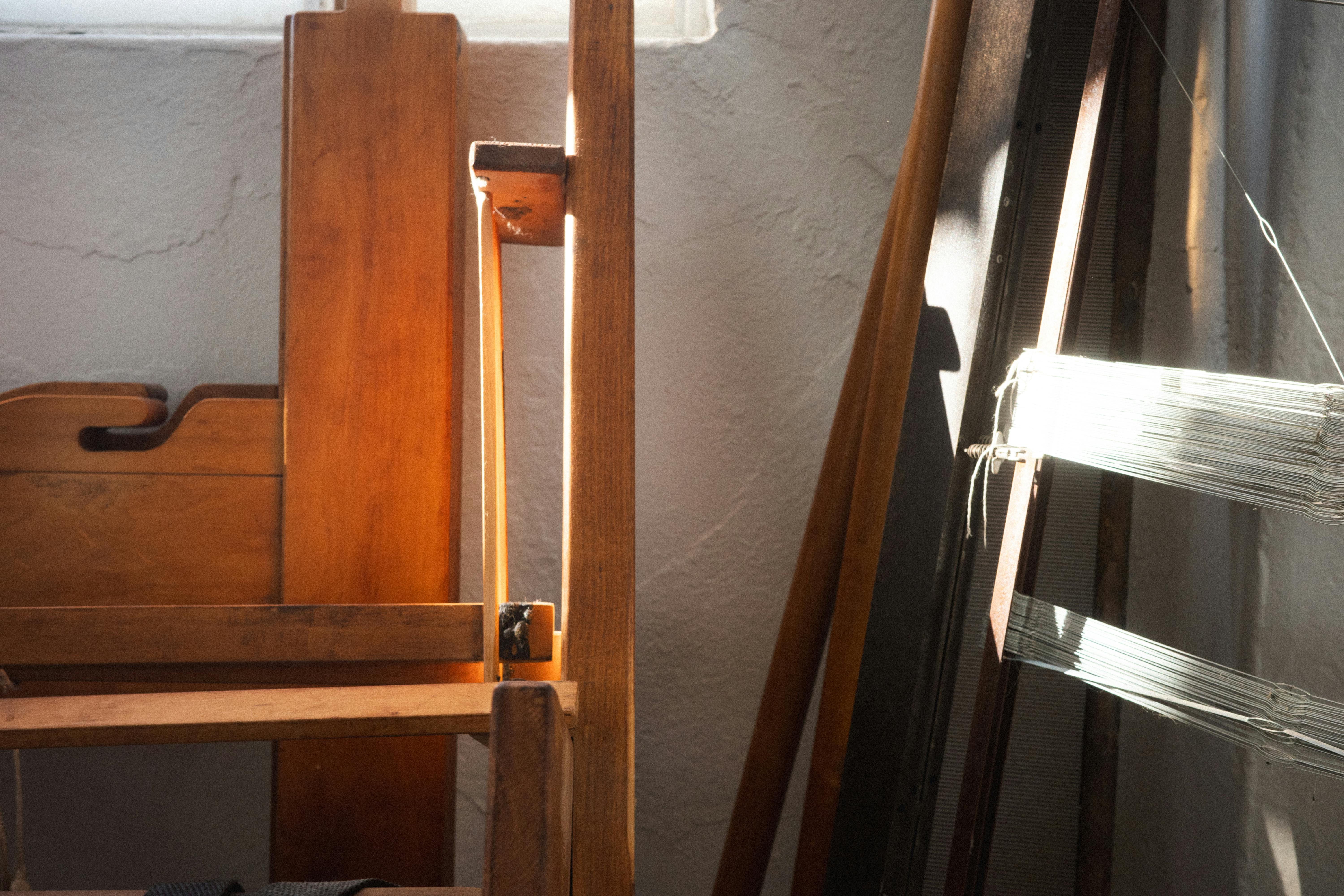 Detail view of a wooden loom with stretched threads catching light inside Sheng Lor’s studio.
