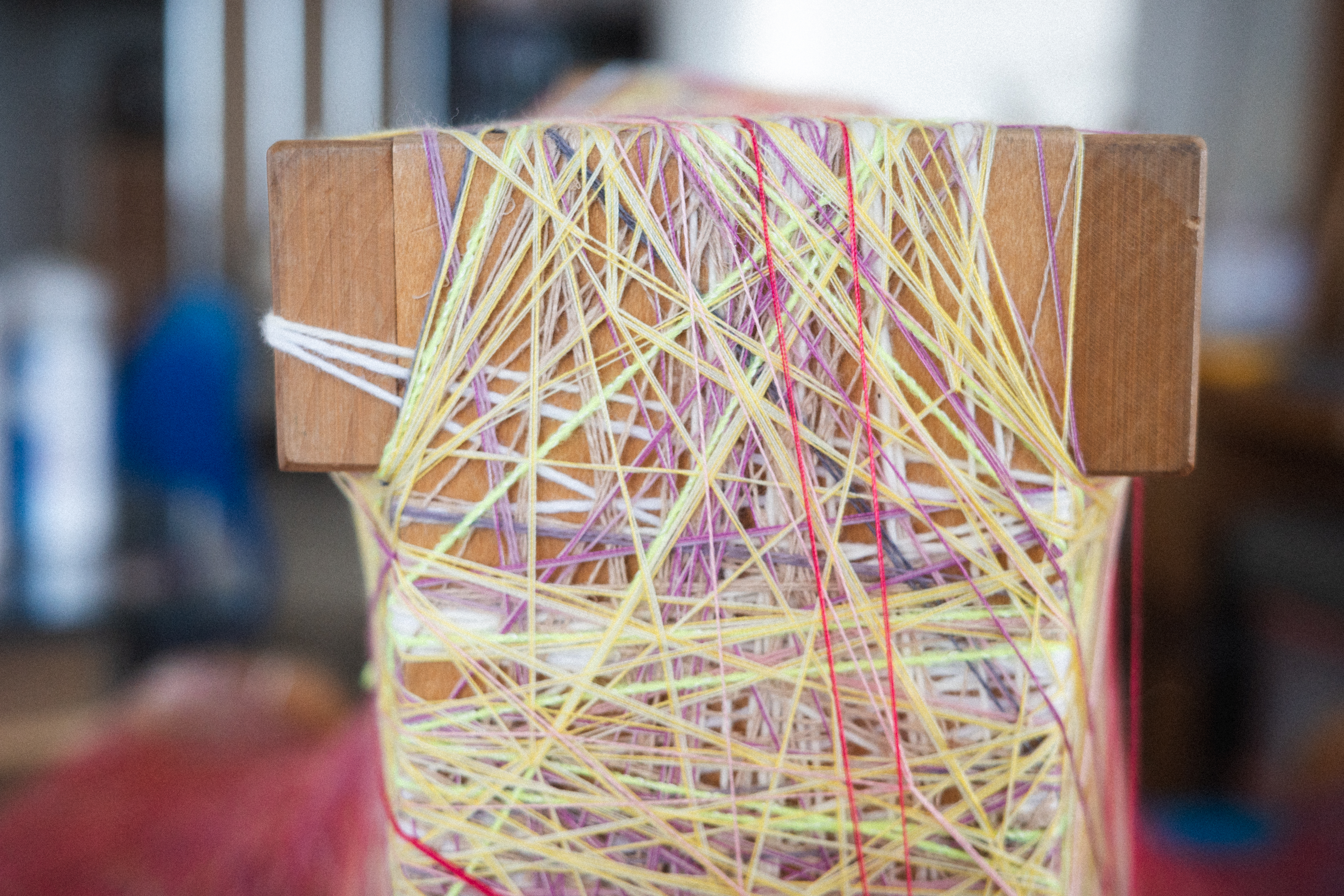 Detail of a wooden loom by Sheng Lor, wrapped with layered pastel threads in yellow, pink, lavender, and white.