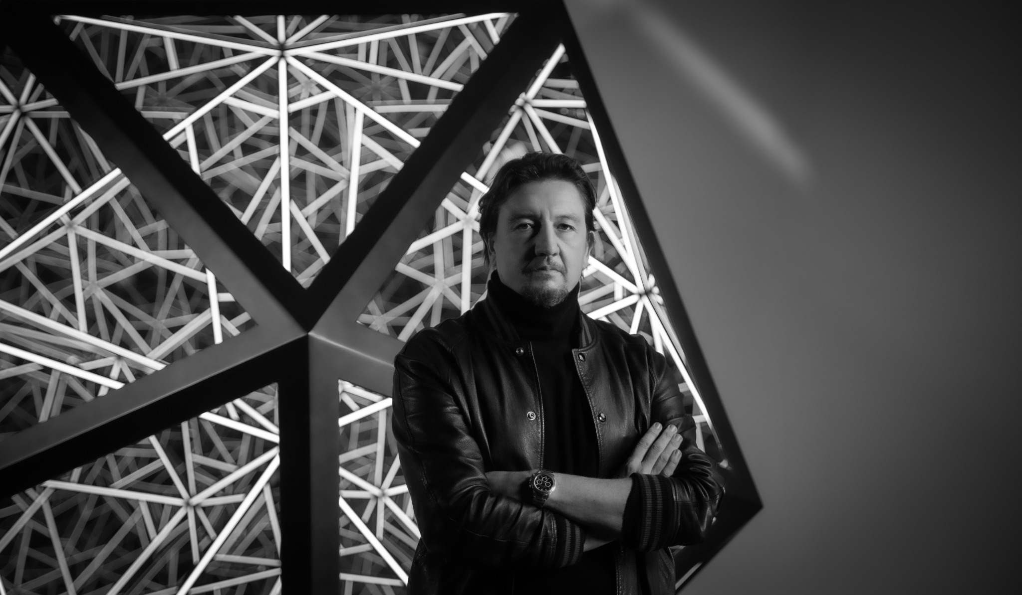 Anthony James standing in his studio with illuminated geometric sculpture behind him, 2025.