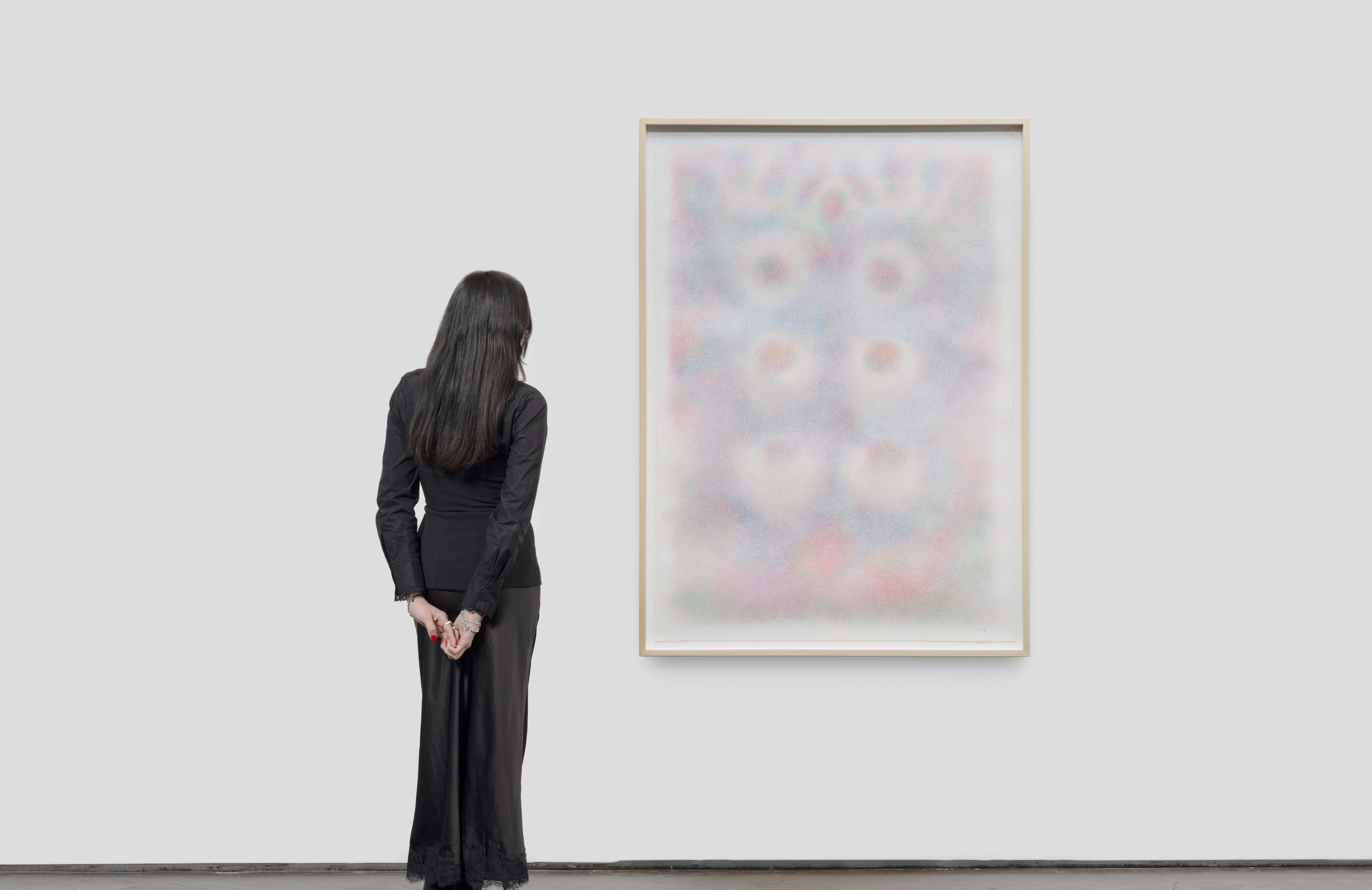 A viewer stands near a framed work in the exhibition, showing the scale of the artwork within the gallery space.
