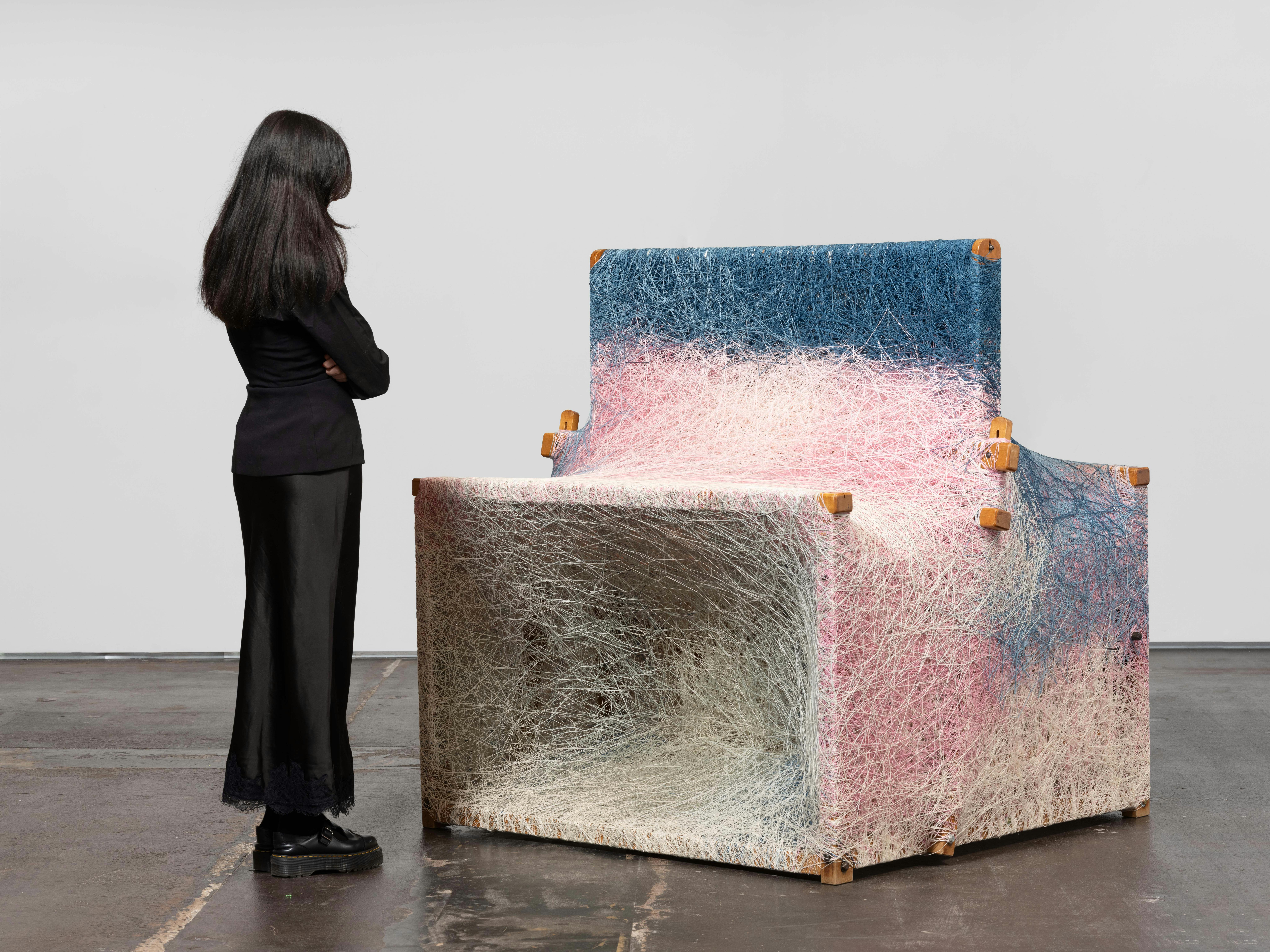 Installation view of Dressed Loom in Repose by Sheng Lor from the exhibition Interstitial at Gallery Sonder, showing a woven sculptural form with a viewer standing nearby for scale.
