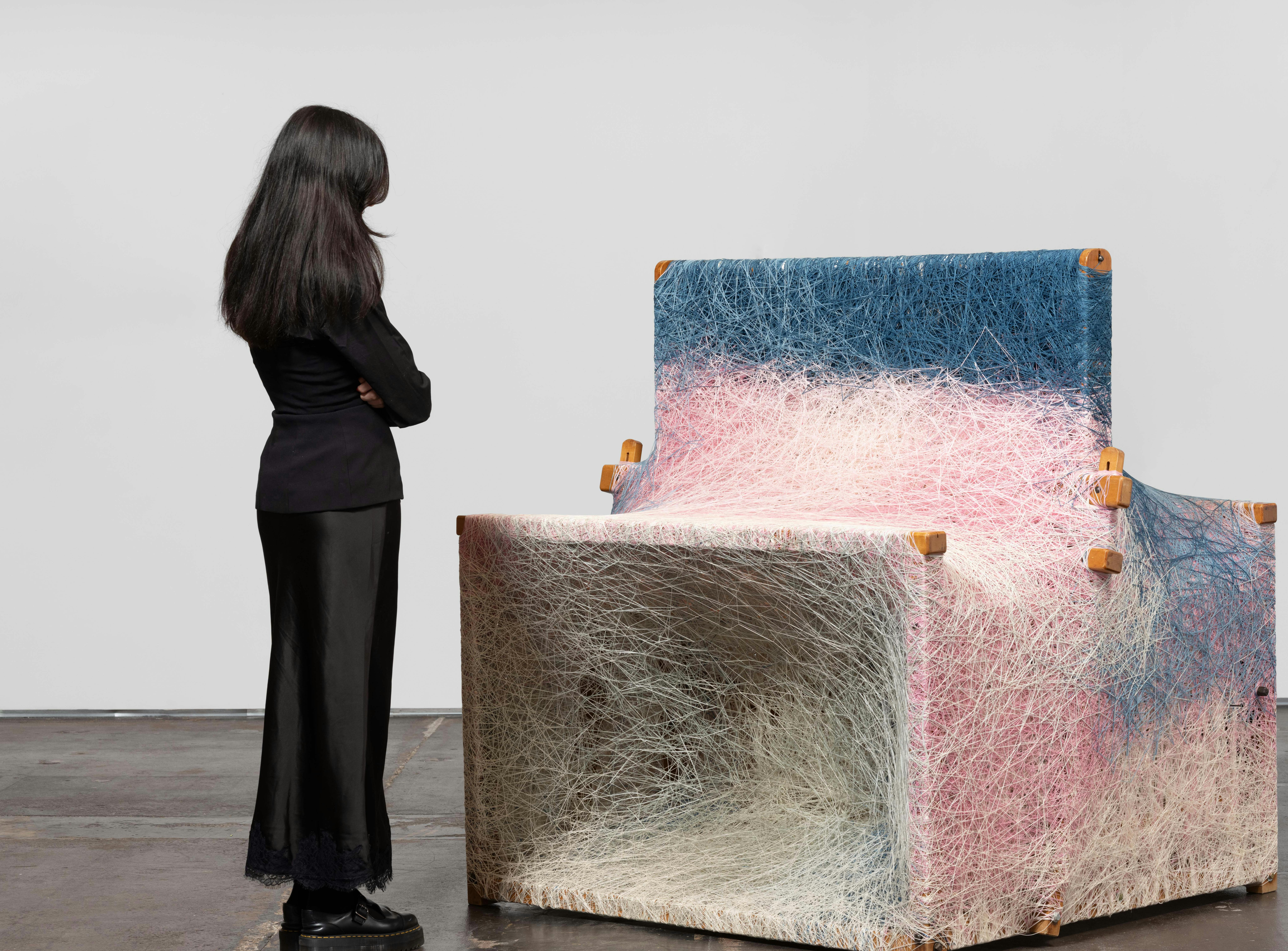 Installation view of Dressed Loom in Repose by Sheng Lor from the exhibition Interstitial at Gallery Sonder, showing a woven sculptural form with a viewer standing nearby for scale.