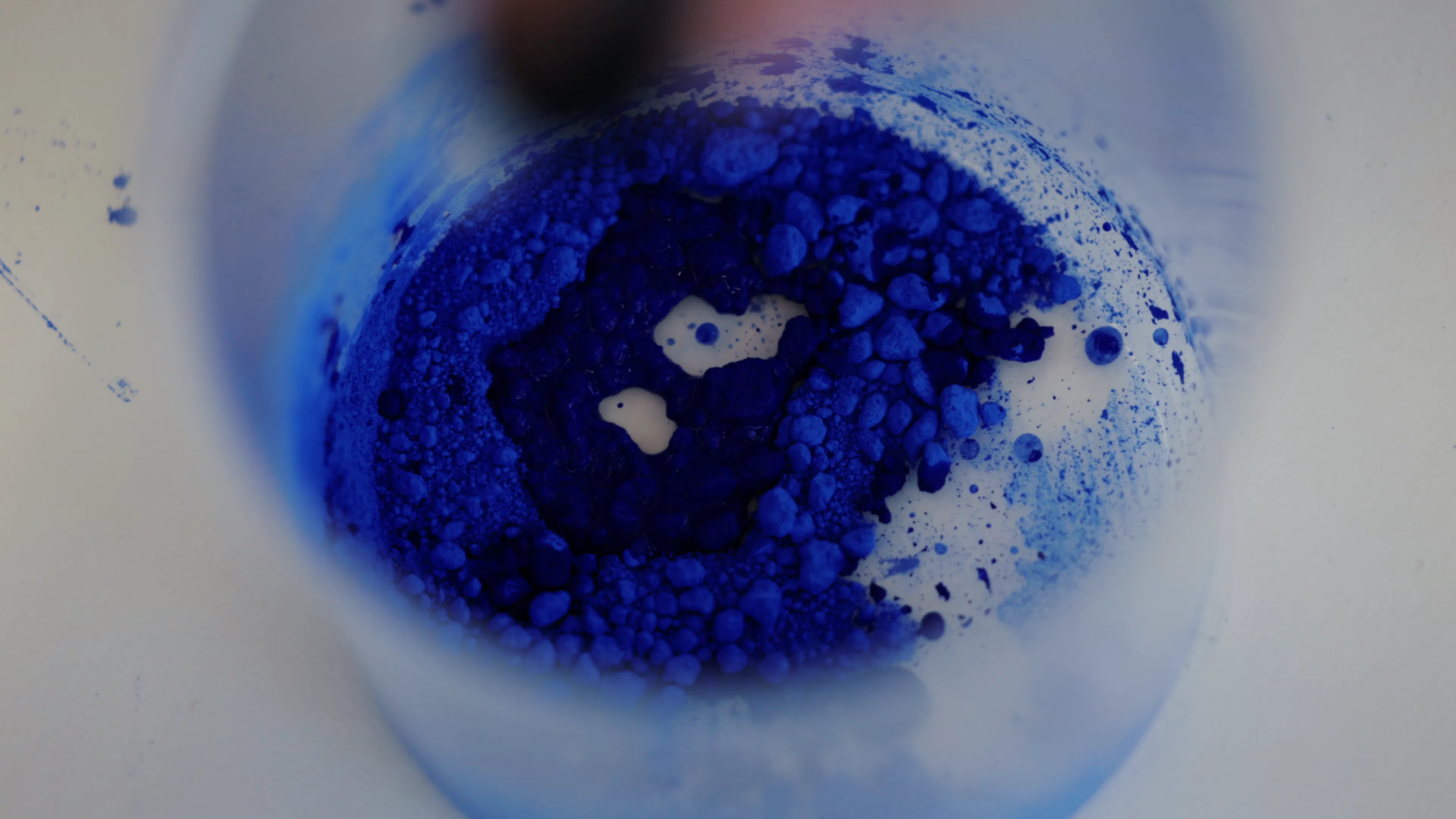 Macro photograph of deep blue pigment mixing in a container used in Ruben Benjamin’s painting process.
