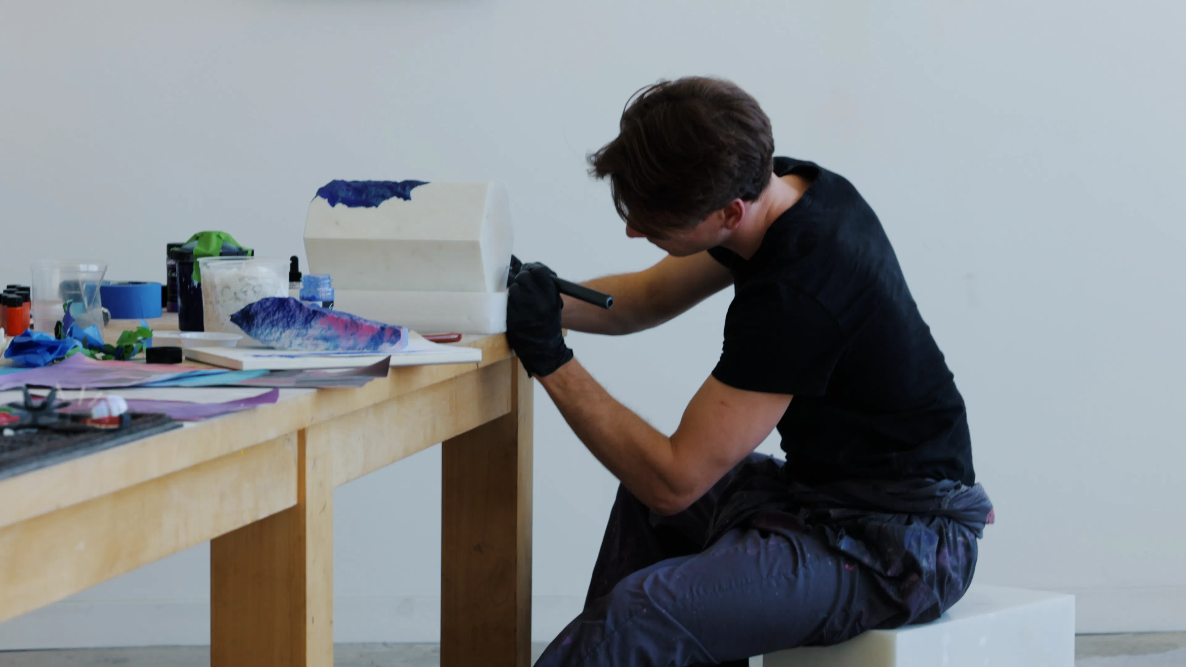 Ruben Benjamin carving a white marble form using a rotary tool in his studio.