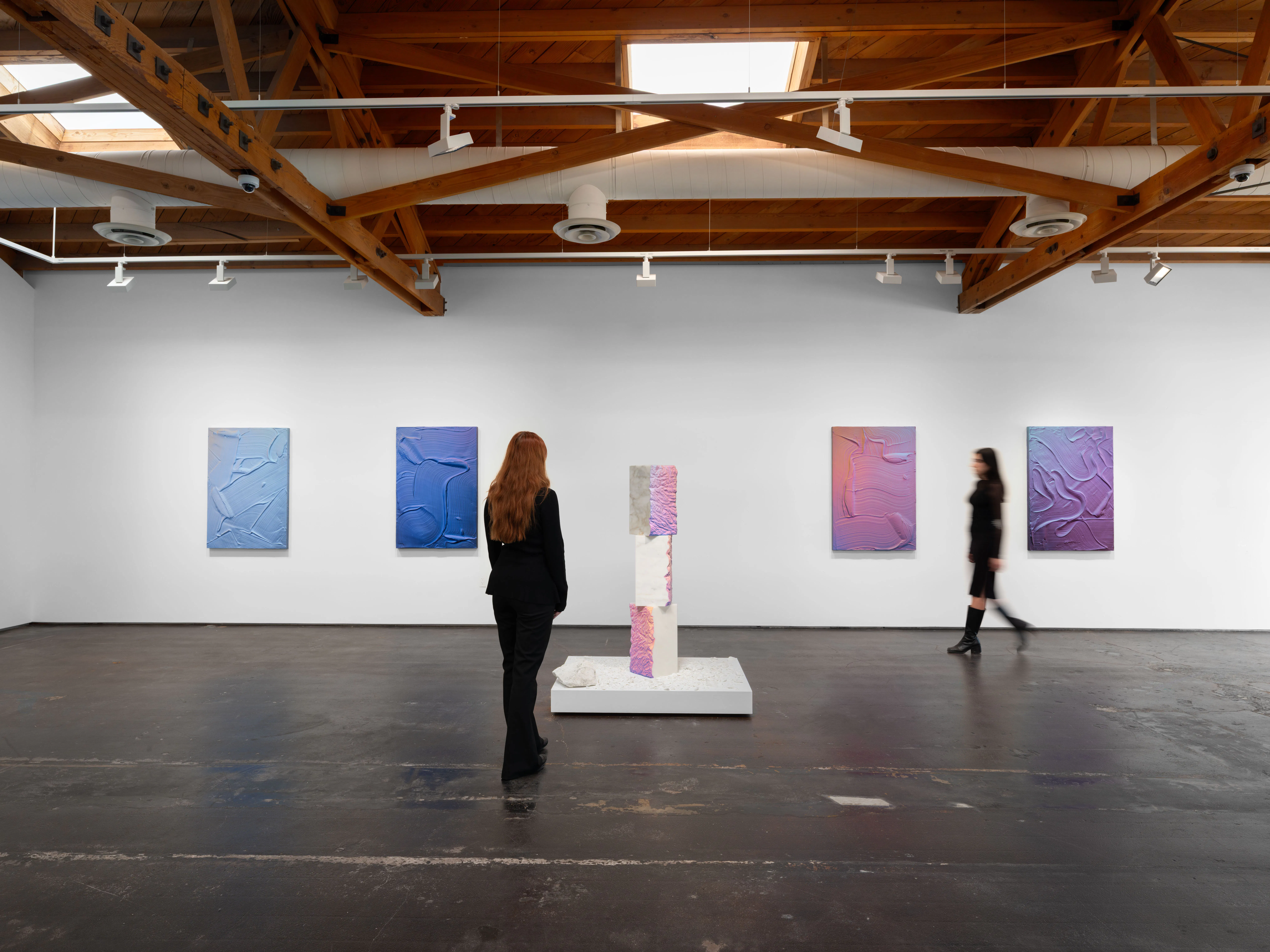 Ruben Benjamin, After The Dust Settles, 2026 — wide installation view at Gallery Sonder showing multiple large-scale paintings across a white wall and a central pedestal sculpture, with two viewers present, emphasizing scale, spatial depth, and material continuity within the gallery. Gallery Sonder, Orange County.
