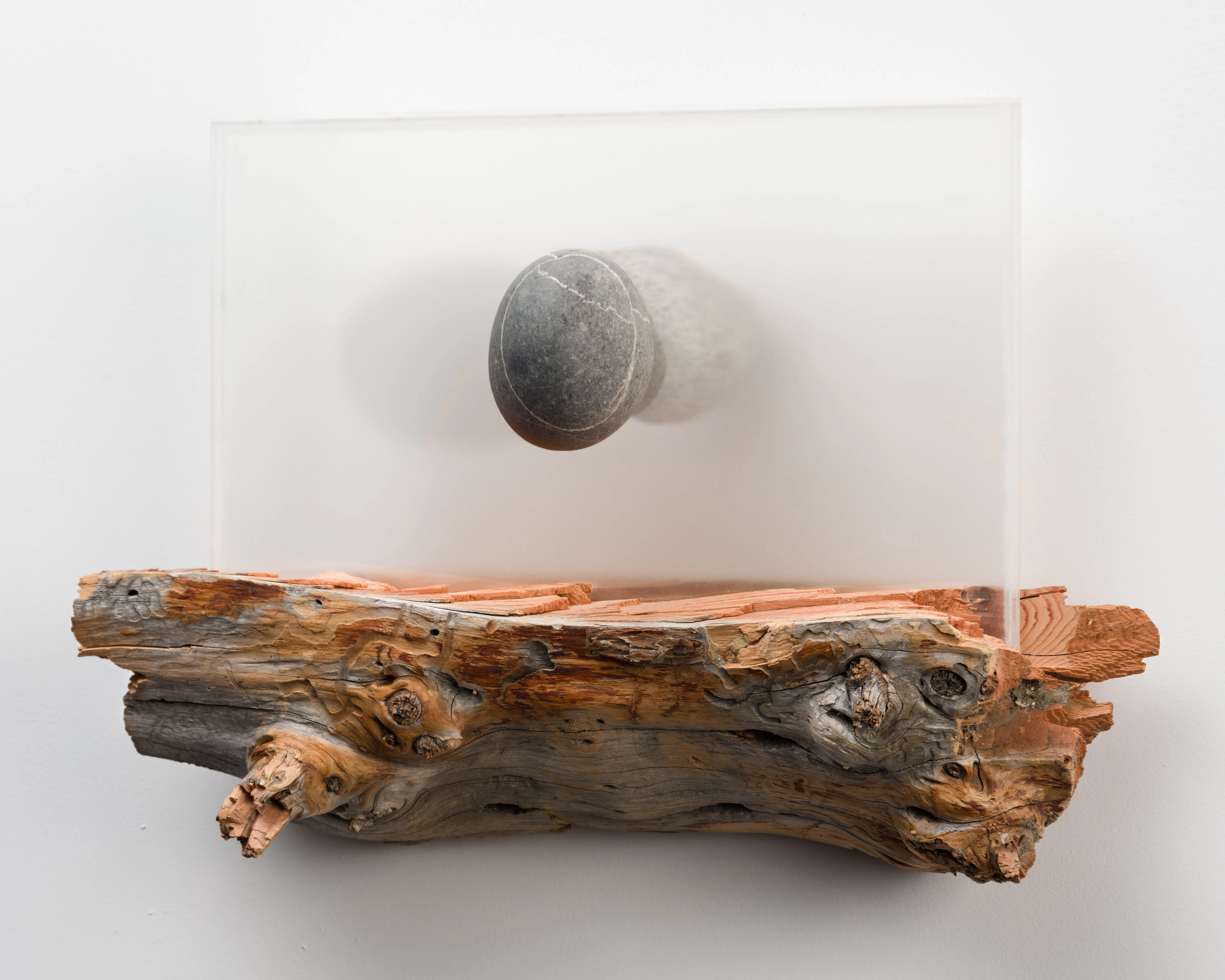Close-up installation detail of a wall-mounted work by Monroe Isenberg combining natural wood, a translucent panel, and a dark circular element.