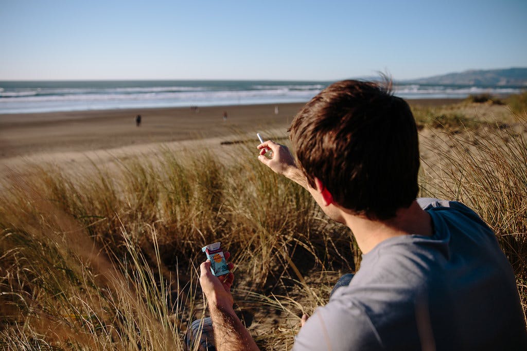 man smoking at the beach and looking out at the water 