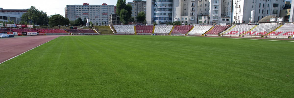 teren de fotbal dinamo cu gazon natural tribune si blocuri in departare