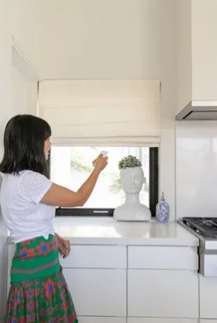 woman opening roman shades in kitchen