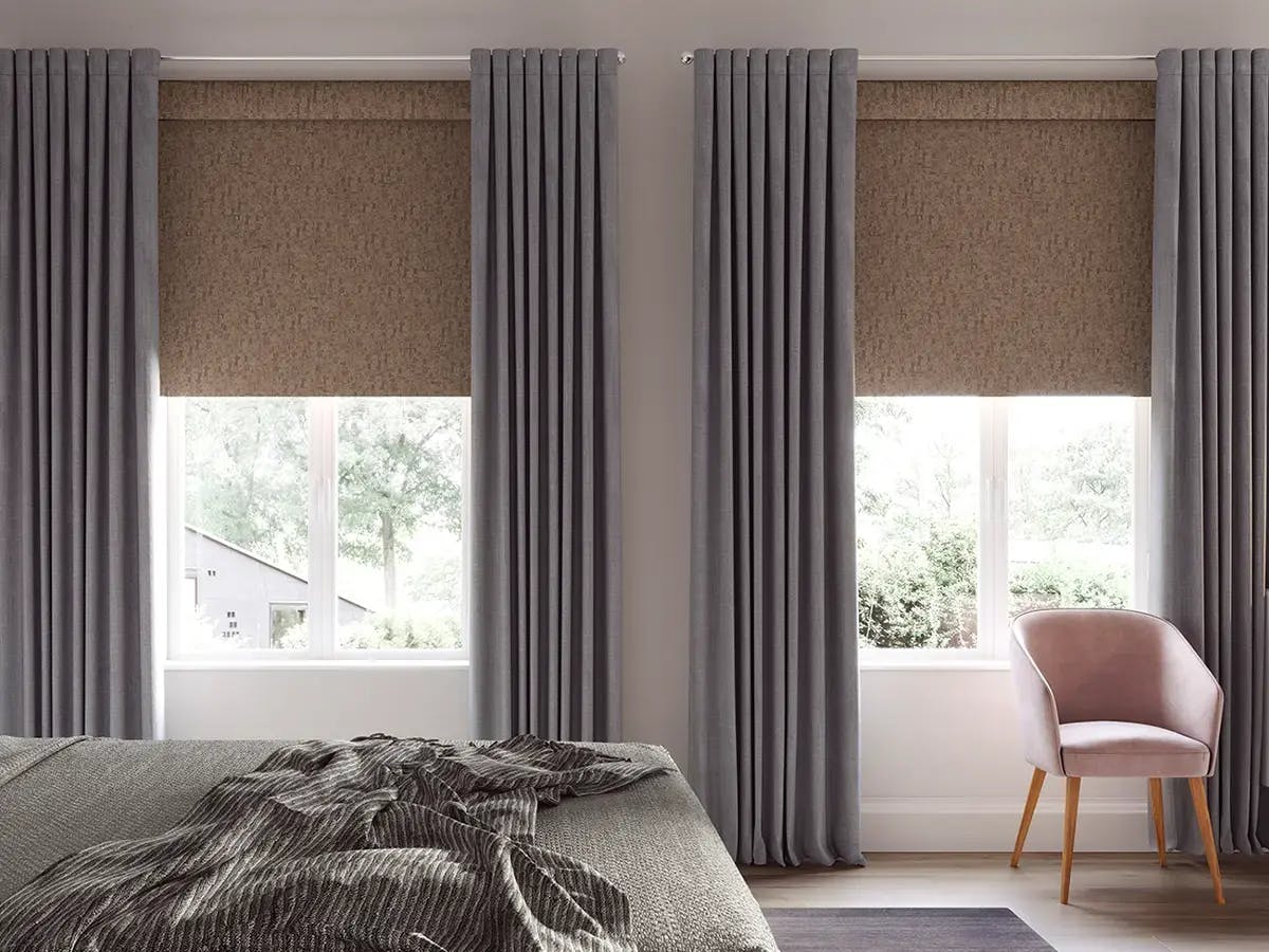 Bedroom features brown roller shades with neutral-colored draperies.