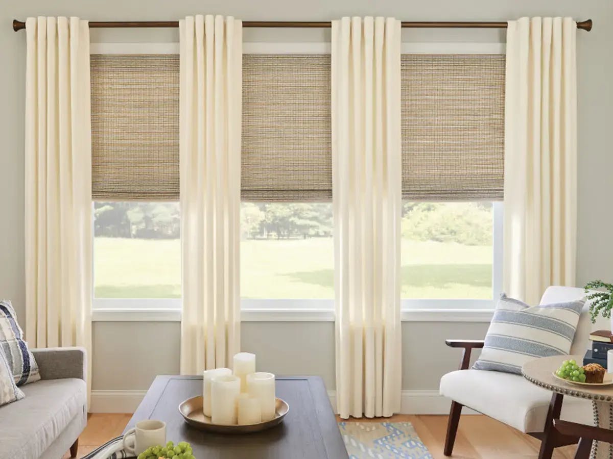 Living room features beige curtains paired with woven shades.