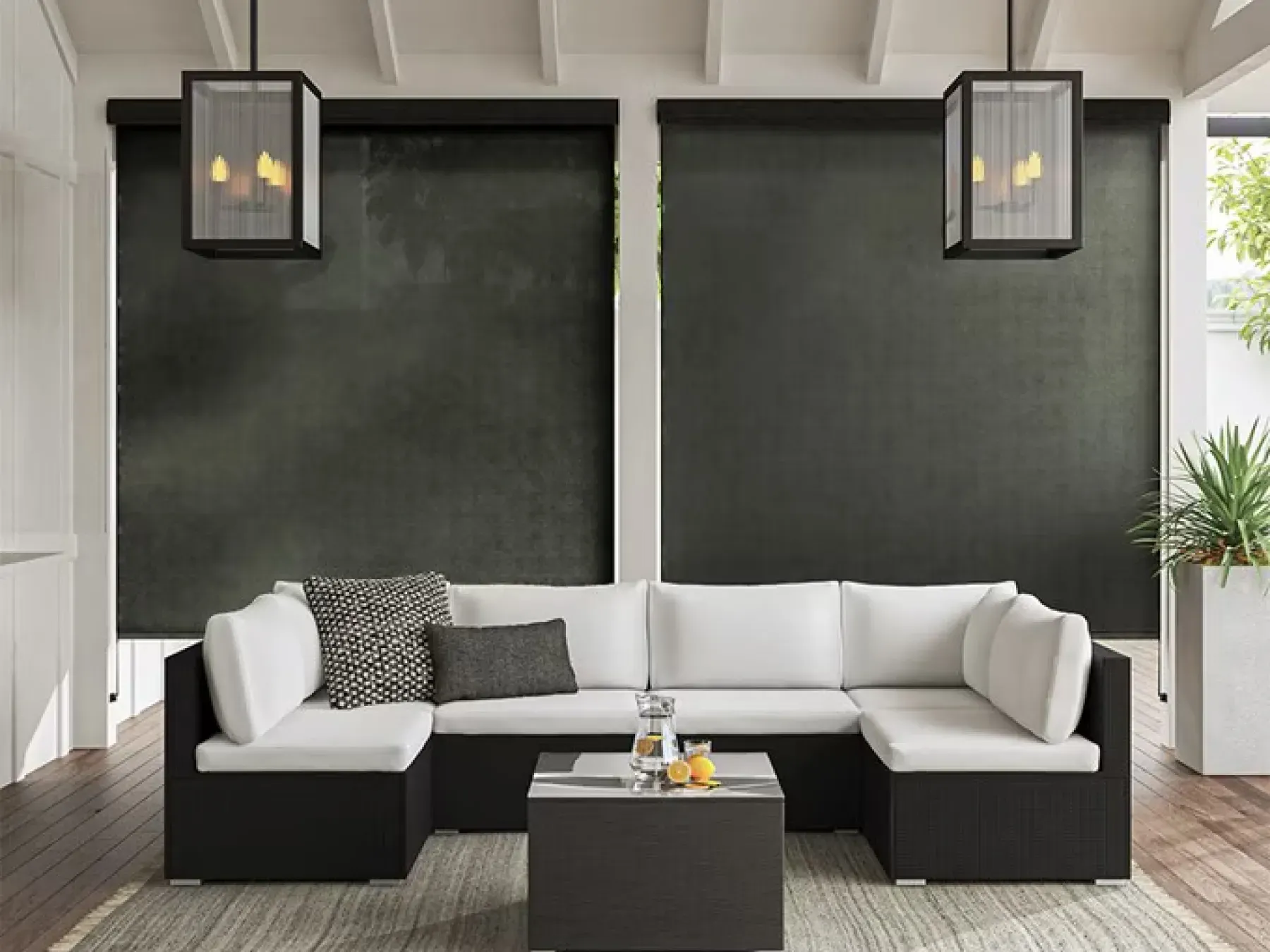 Outdoor living space with a black and white color scheme. The outdoor couch has a black base and white cushions. Behind the couch are two black outdoor solar shades pulled all the way down. Above the couch are two geometric lanterns.