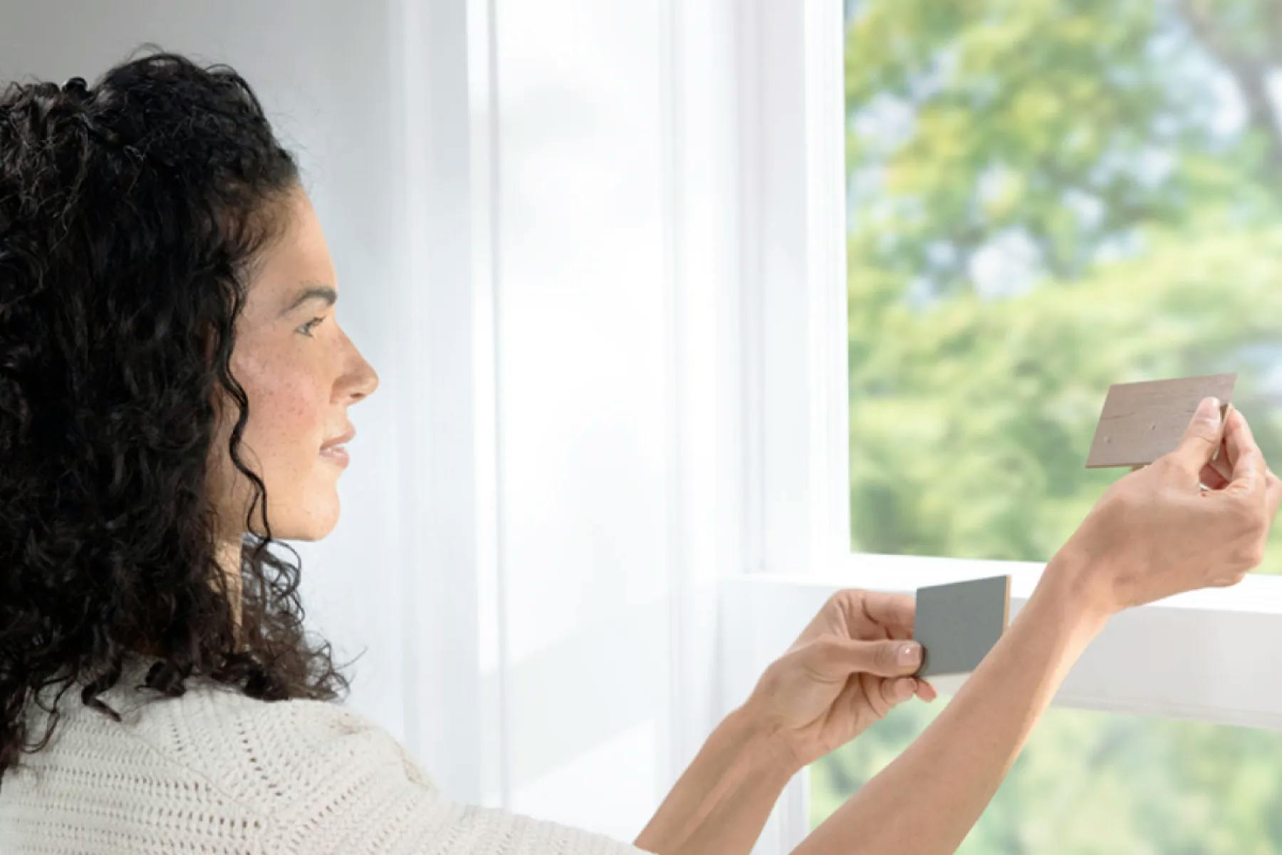 Woman holding up two faux wood samples in front of her window.
