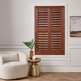 Living room featuring rich wooden plantation shutters framed by white molding, paired with a modern cream chair and gold accent table.