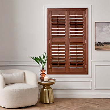 Living room featuring rich wooden plantation shutters framed by white molding, paired with a modern cream chair and gold accent table.