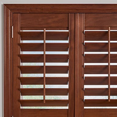 Living room featuring rich wooden plantation shutters framed by white molding, paired with a modern cream chair and gold accent table.