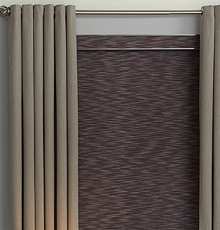 Bedroom with elegant floor-length gray drapes layered over textured blackout roller shades, styled beside a modern black console table and lamp
