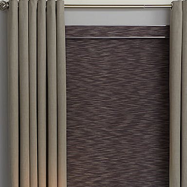 Bedroom with elegant floor-length gray drapes layered over textured blackout roller shades, styled beside a modern black console table and lamp