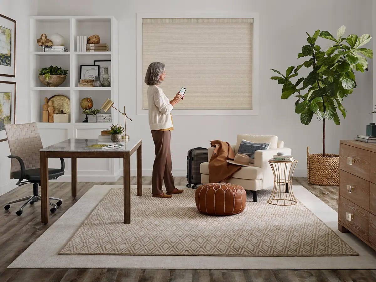 A person standing in a modern home office with neutral décor and a large window shade.