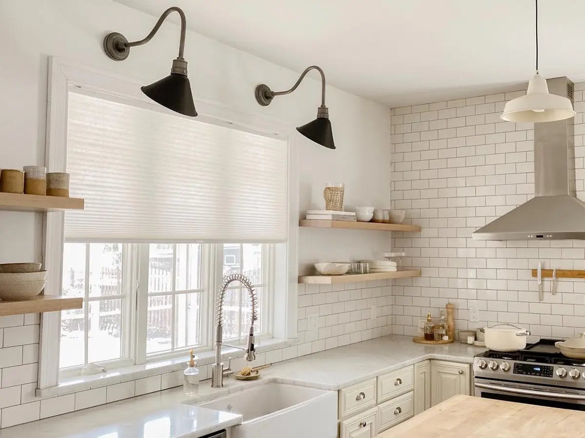 A bright kitchen with open wooden shelves and a cellular window shade above the sink.