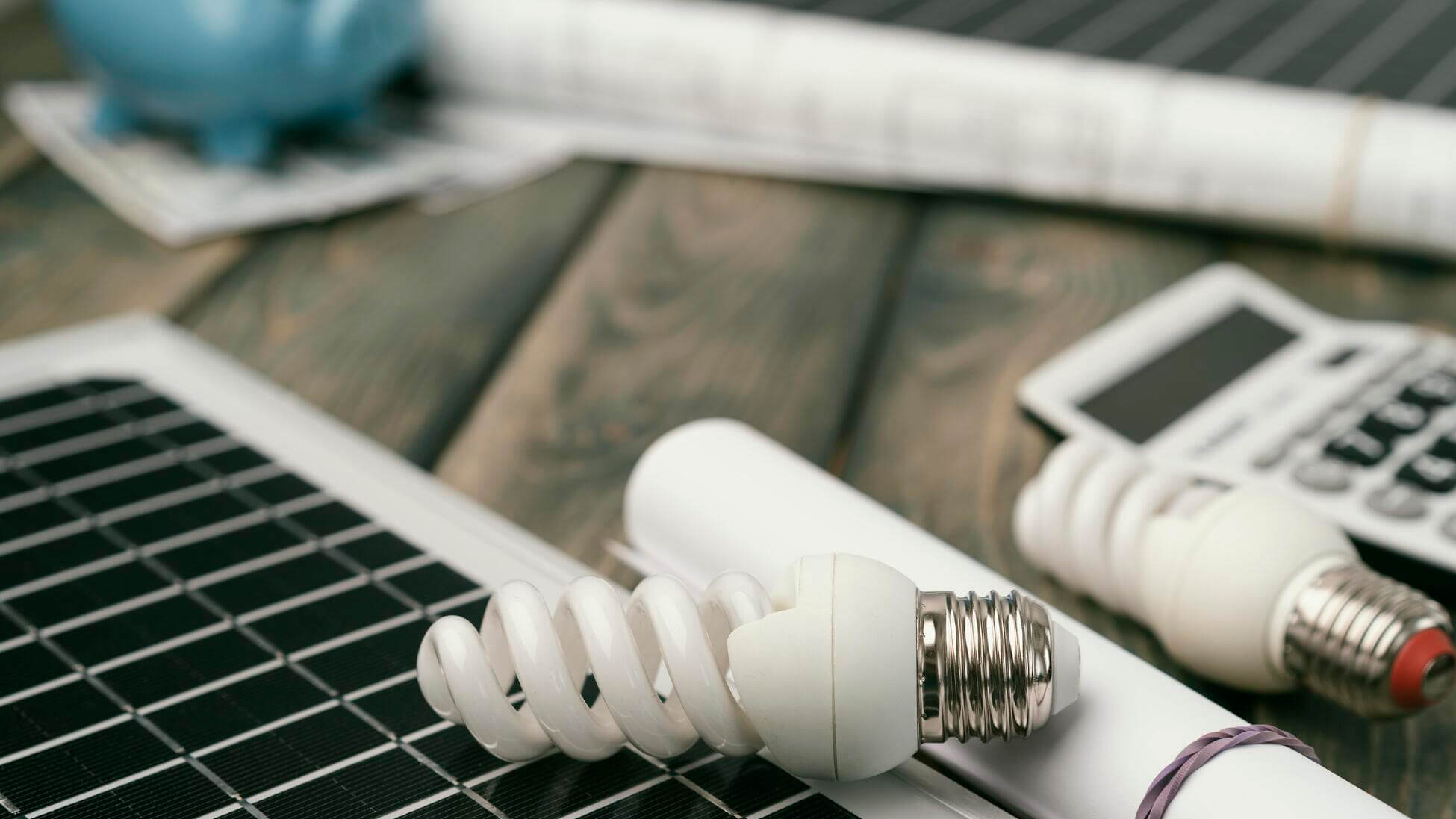 Solarmodul und Energiesparlampen auf einem Tisch mit Taschenrechner und Sparschwein im Hintergrund, bei der Berechnung des Eigenverbrauchs | Gelb Solar