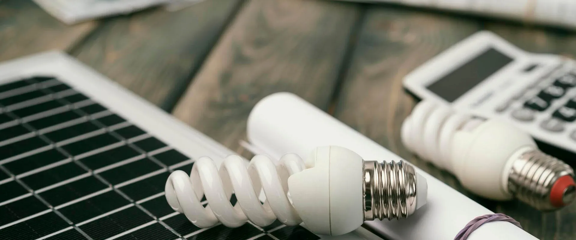 Solarmodul und Energiesparlampen auf einem Tisch mit Taschenrechner und Sparschwein im Hintergrund, bei der Berechnung des Eigenverbrauchs | Gelb Solar