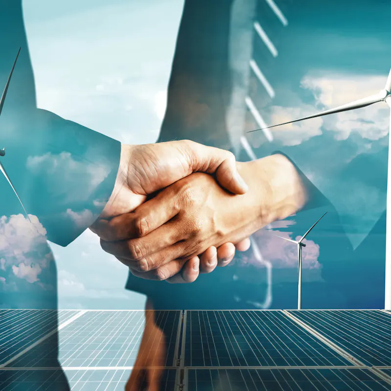 Zwei Geschäftsleute im Anzug geben sich die Hand, im Hintergrund überlagert eine Szenerie mit Windkraftanlagen, Solarpanels und blauem Himmel mit Wolken – Symbolbild für Zusammenarbeit und Investition beim Energy Sharing in Deutschland Zwei Geschäftsleute im Anzug geben sich die Hand, im Hintergrund überlagert eine Szenerie mit Windkraftanlagen, Solarpanels und blauem Himmel mit Wolken – Symbolbild für Zusammenarbeit und Investition beim Energy Sharing in Deutschland