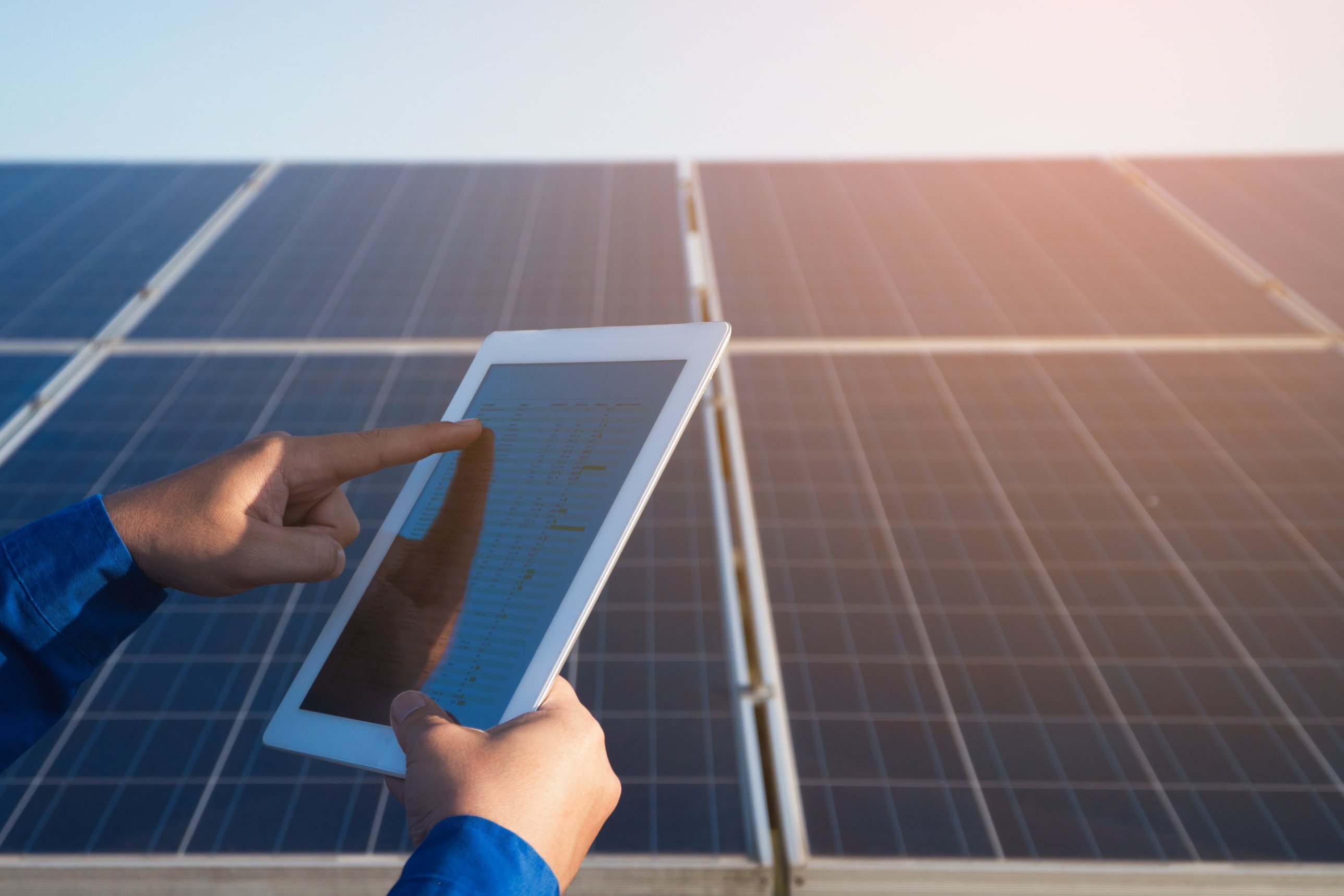 Person prüft den Solarertrag der PV-Anlage auf einem Tablet vor Solarmodulen