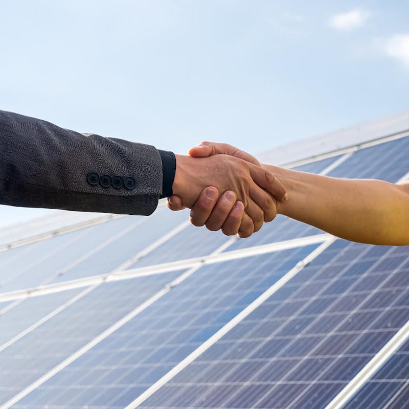 Handschlag zwischen zwei Personen vor einer Photovoltaikanlage – symbolisch für Partnerschaft, Investition und Vertrauen im Bereich erneuerbare Energien